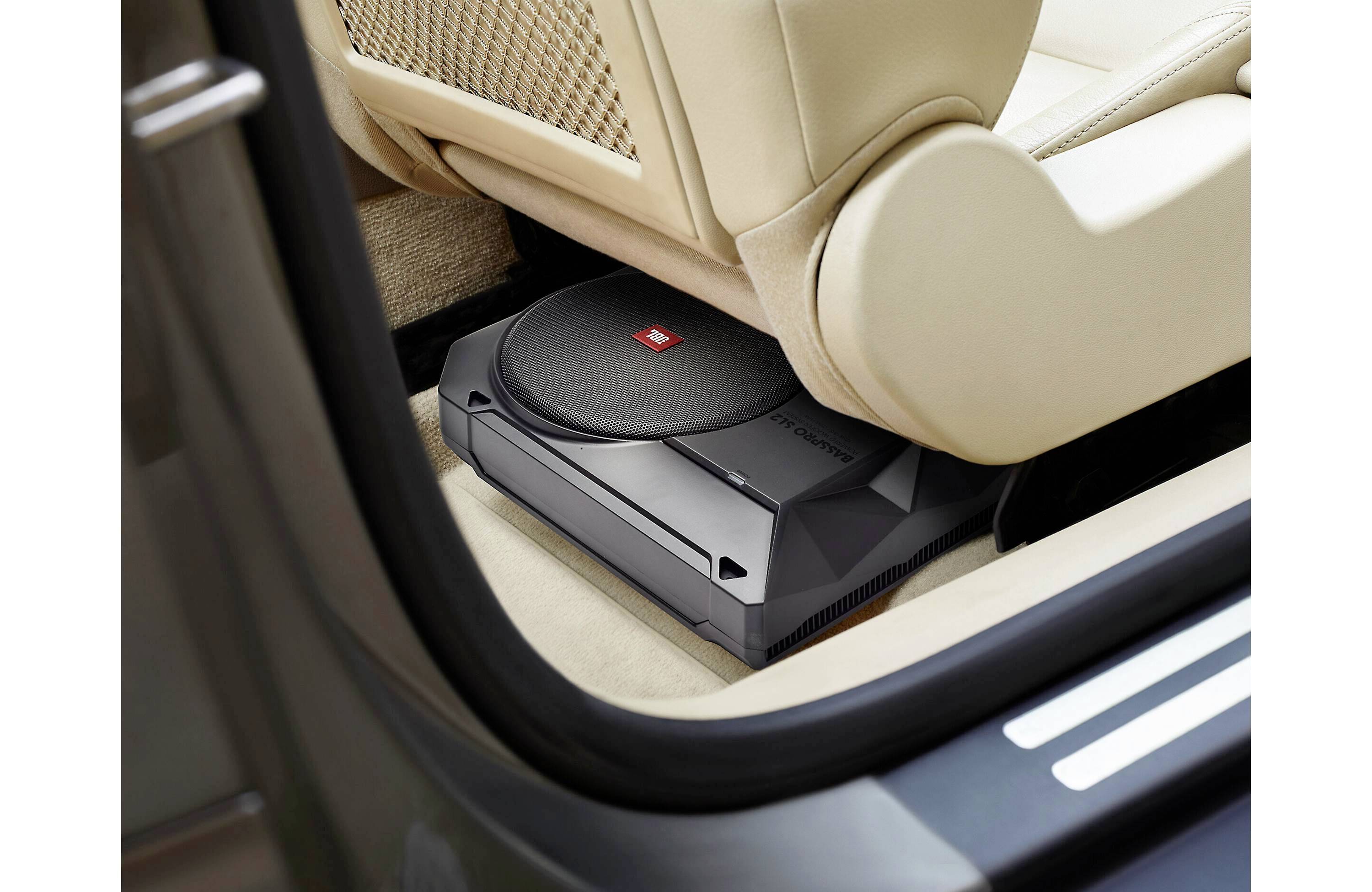 Czarny subwoofer jest zamontowany i widoczny pod beżowym fotelem samochodowym, gdy drzwi samochodu są otwarte.