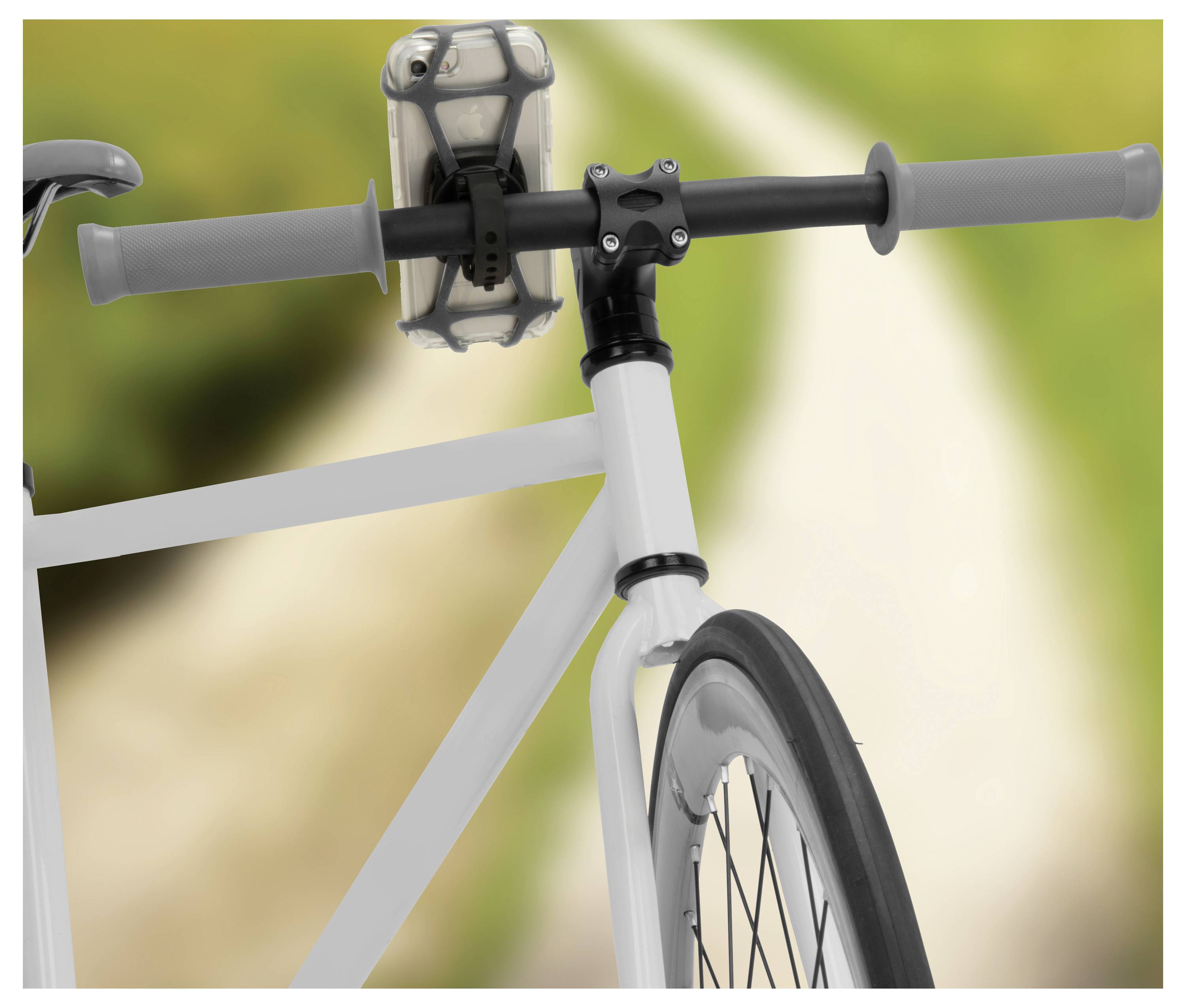 Kierownica roweru z zamontowanym uchwytem na smartfona jest widoczna na tle rozmytego krajobrazu przyrodniczego, sugerując trasę rowerową.