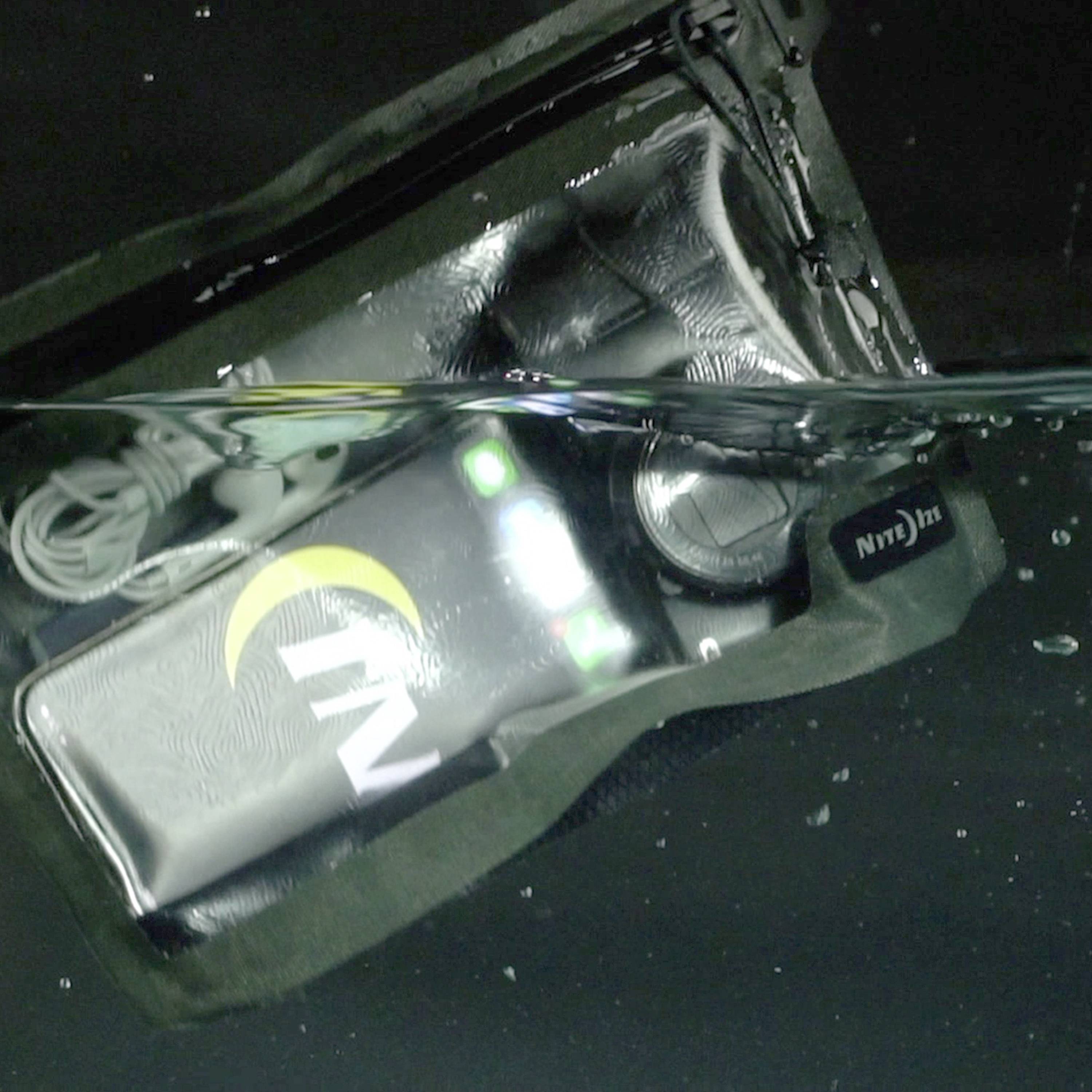 Wodoodporny telefon z podświetlanym wyświetlaczem leży w zbiorniku napełnionym wodą.