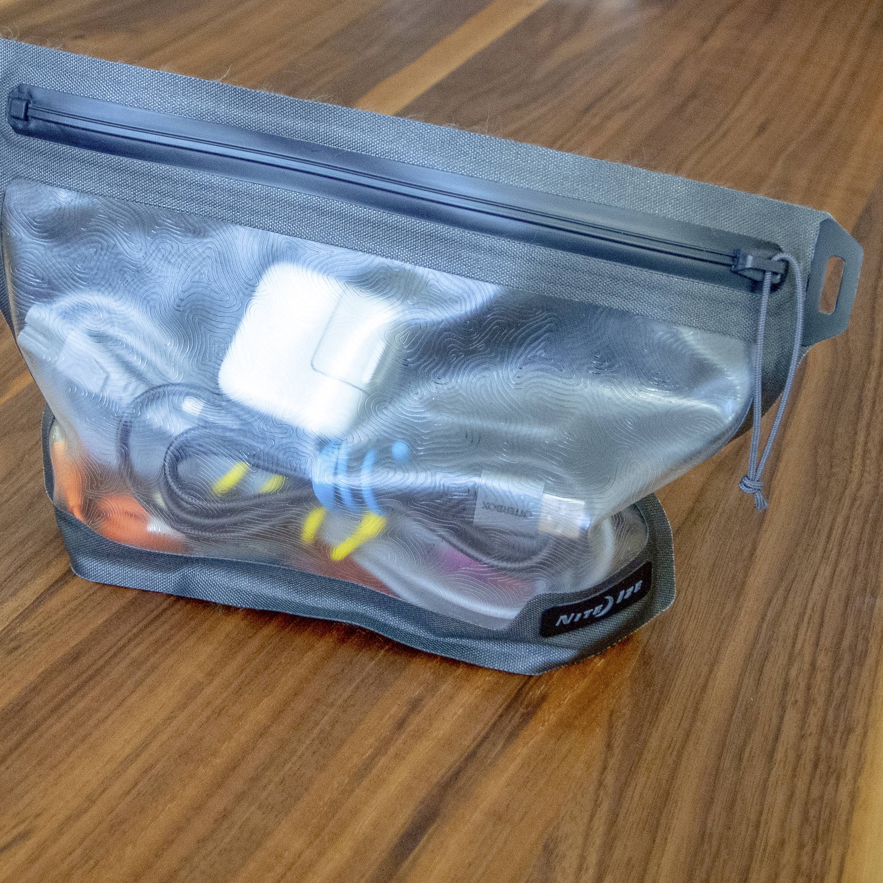 Przezroczysta torba na drewnianym stole, wypełniona akcesoriami elektronicznymi, takimi jak kable ładujące i adaptery.