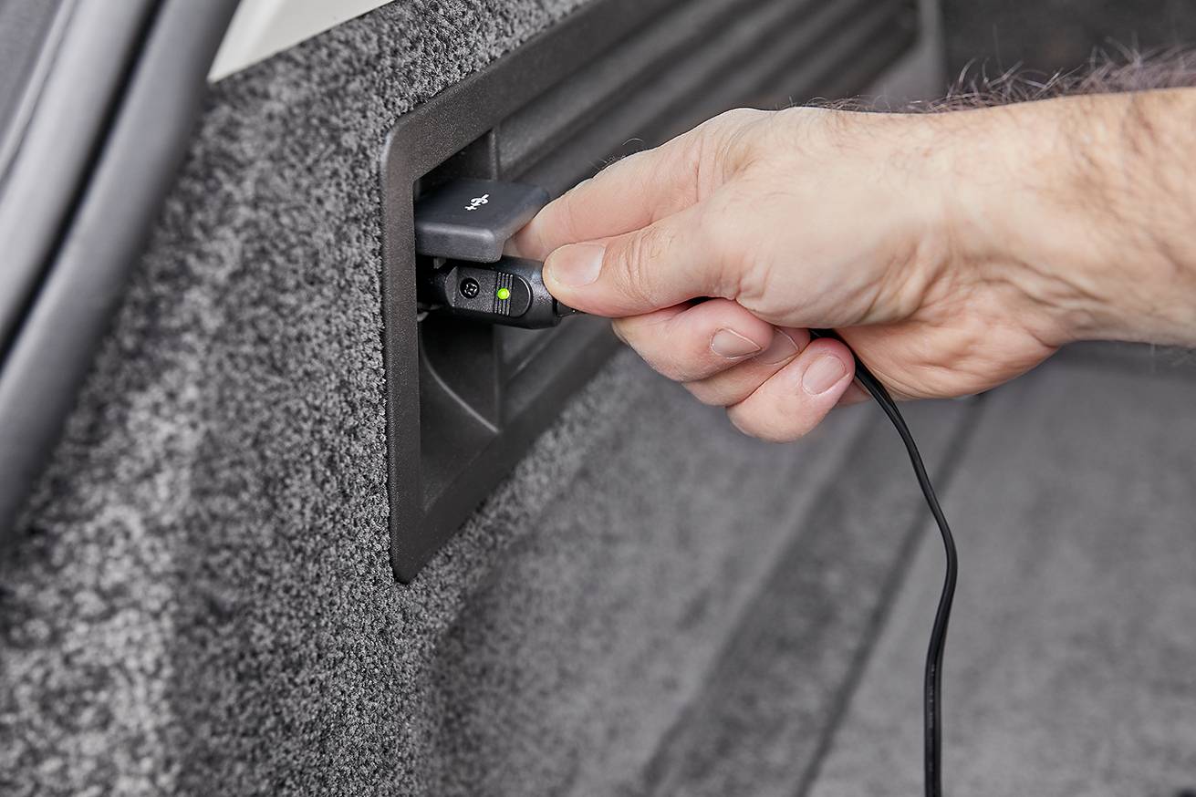 Osoba podłącza kabel USB w bagażniku samochodu. Ręka wkłada wtyczkę w ścianę, fokus na złączu. Tło rozmyte.