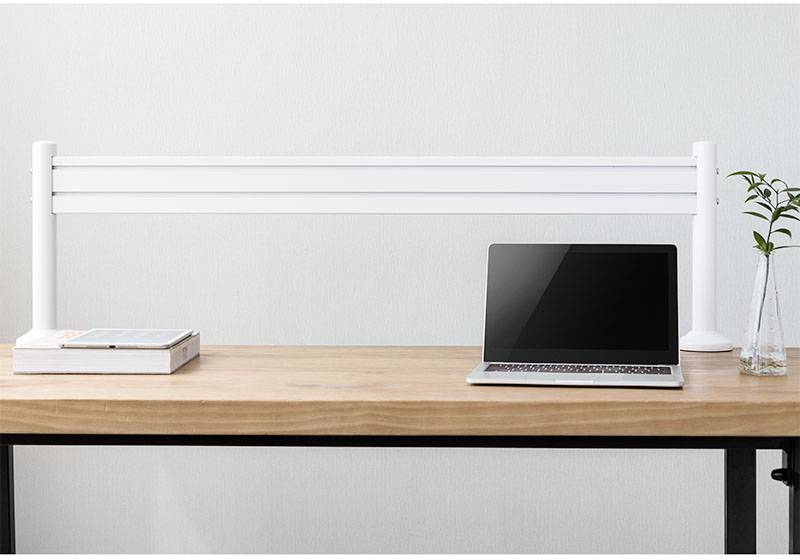 Laptop jest otwarty i stoi na drewnianym biurku. Obok niego leży stos książek i smukła waza z rośliną.