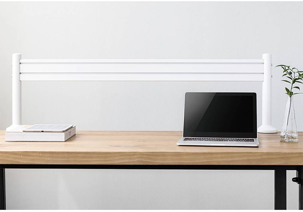 Na stole stoi otwarty laptop obok stosu książek i przezroczystego wazonu z małą rośliną. Za laptopem znajduje się prosta biała ścianka działowa.