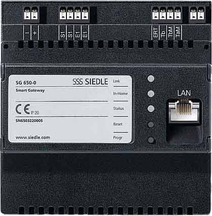 SBP Siedle SG 650-0 Smart Gateway. Czarne urządzenie z portem LAN i kilkoma zaciskami przyłączeniowymi u góry. Numer modelu i numer seryjny po lewej stronie na etykiecie.