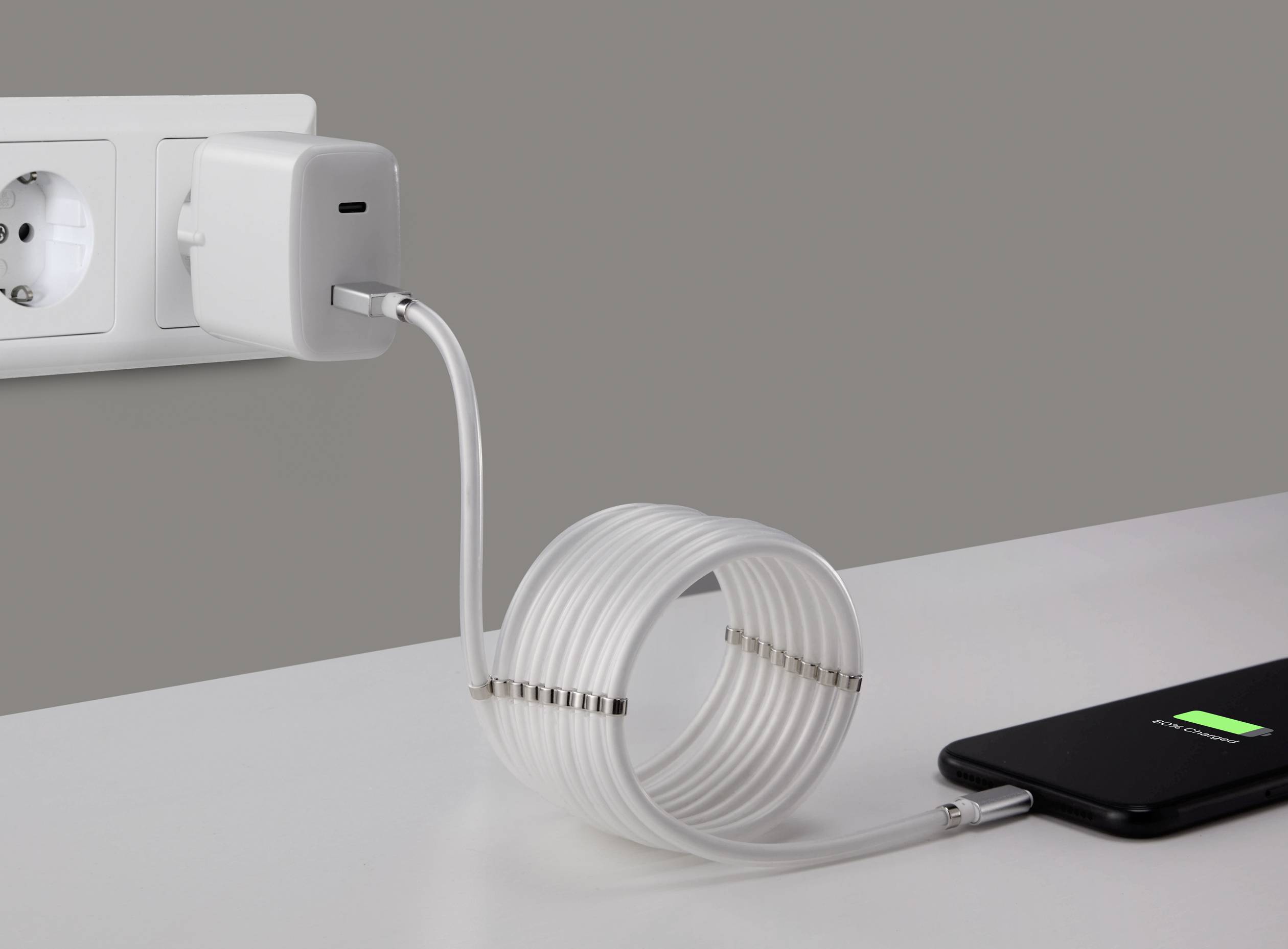 Smartfon ładuje się na stole. Biały kabel łączy telefon z ładowarką, która jest podłączona do gniazdka elektrycznego.