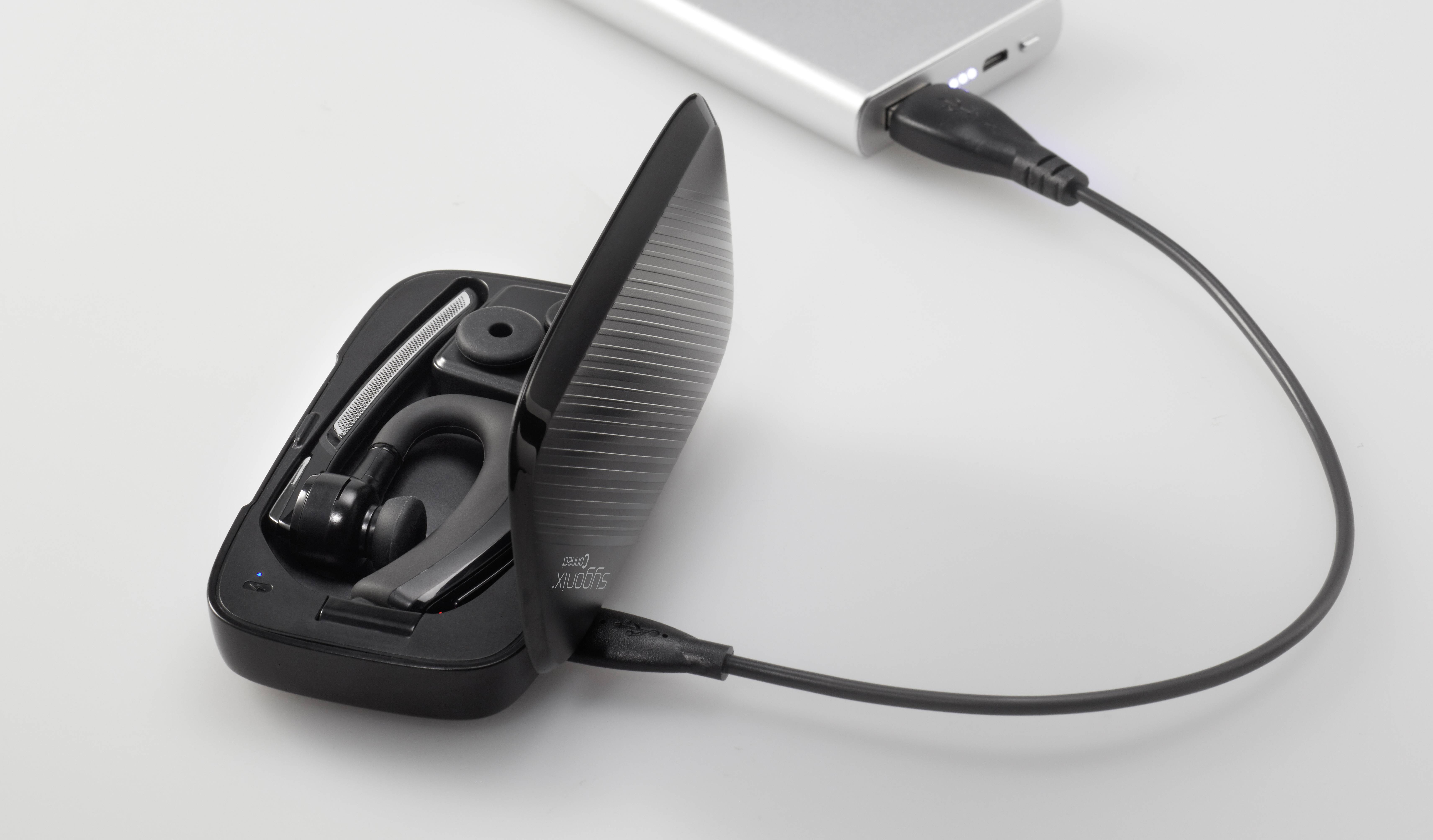 Otwarte etui ładujące z bezprzewodową słuchawką douszną, podłączone do kabla ładującego, który jest podłączony do osobnego źródła zasilania.