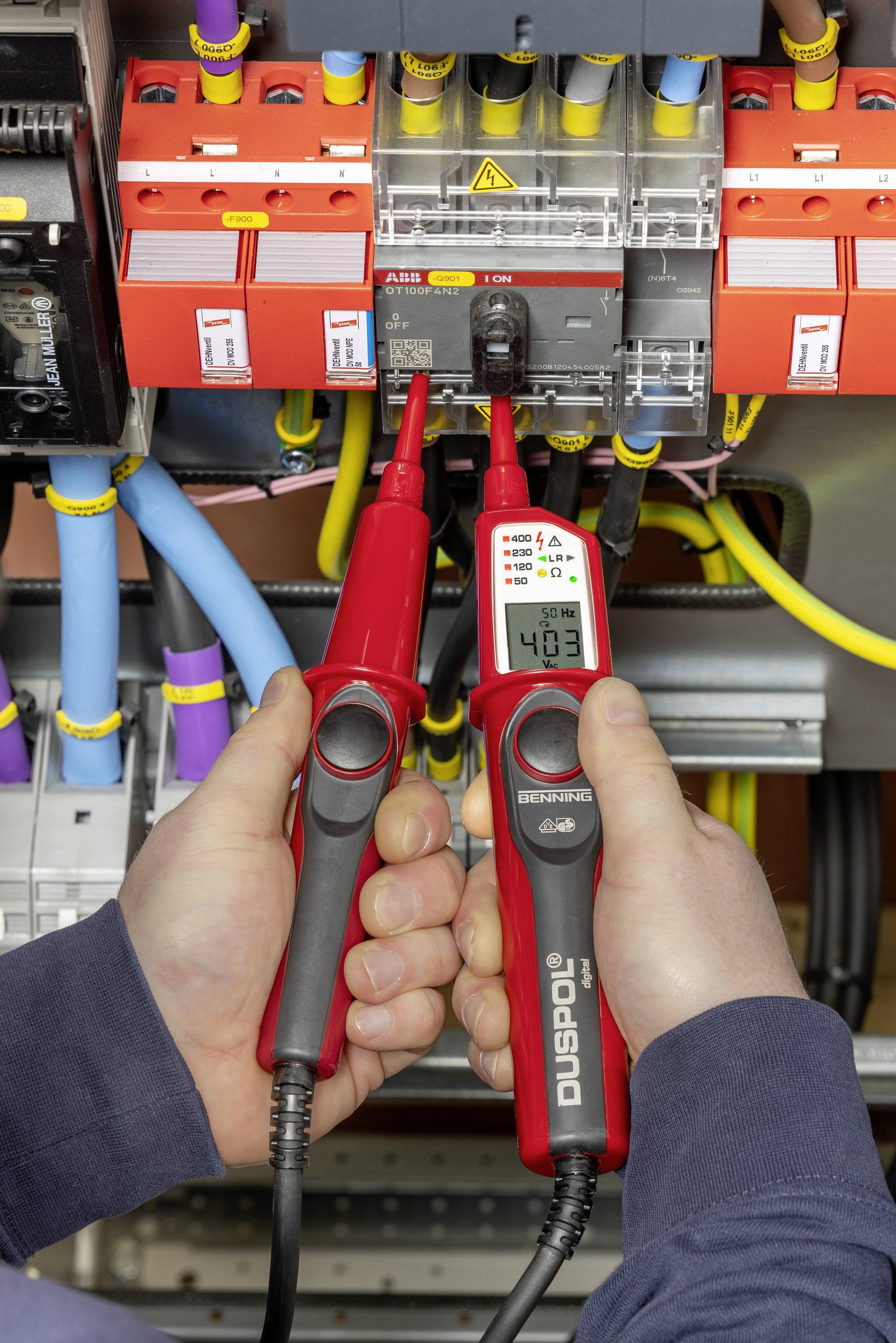 Elektryk używa miernika napięcia, aby zmierzyć napięcie w rozdzielnicy elektrycznej. Wyświetlacz pokazuje '403 V'.