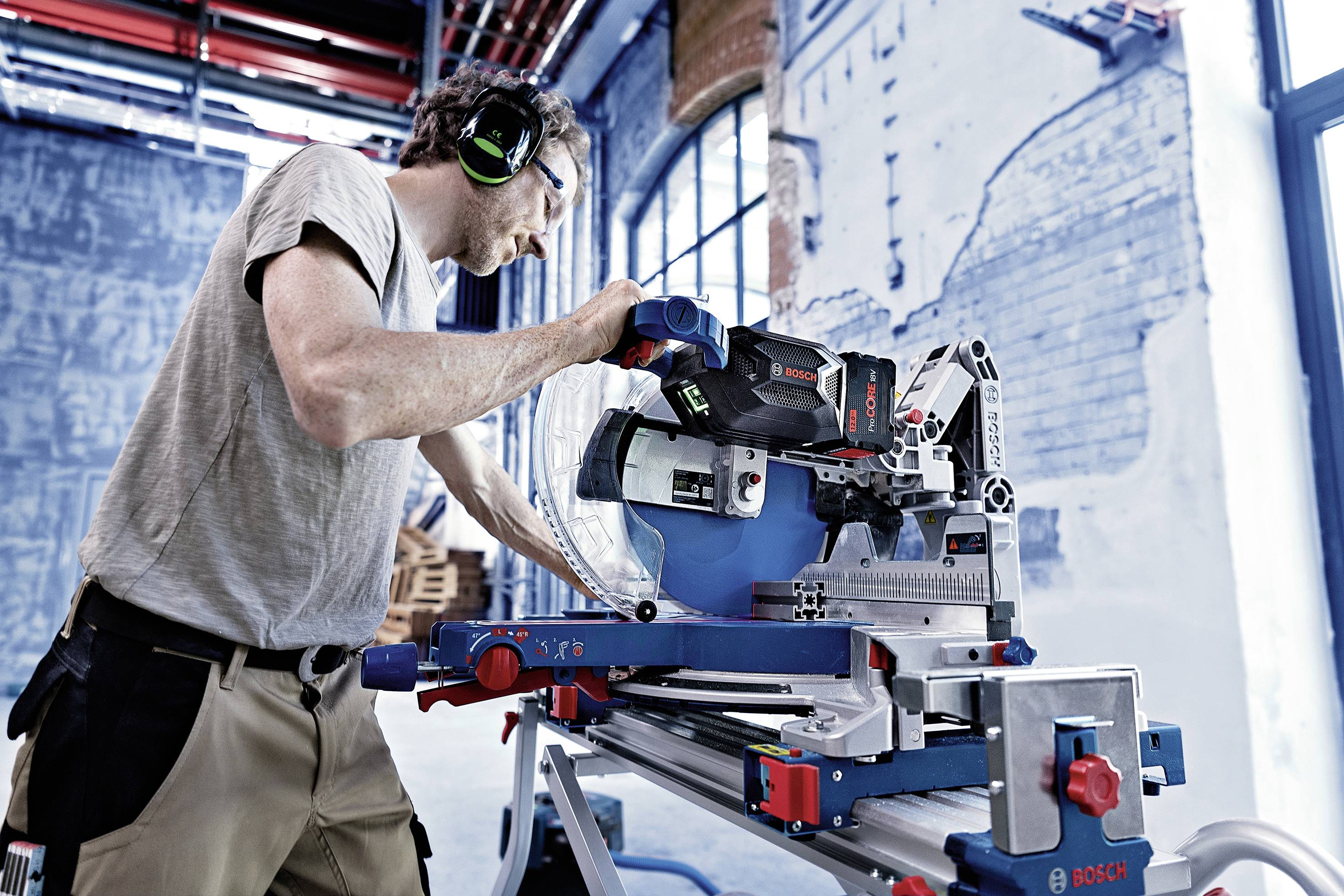 Mężczyzna w ochronnikach słuchu obsługuje piłę tarczową w warsztacie.