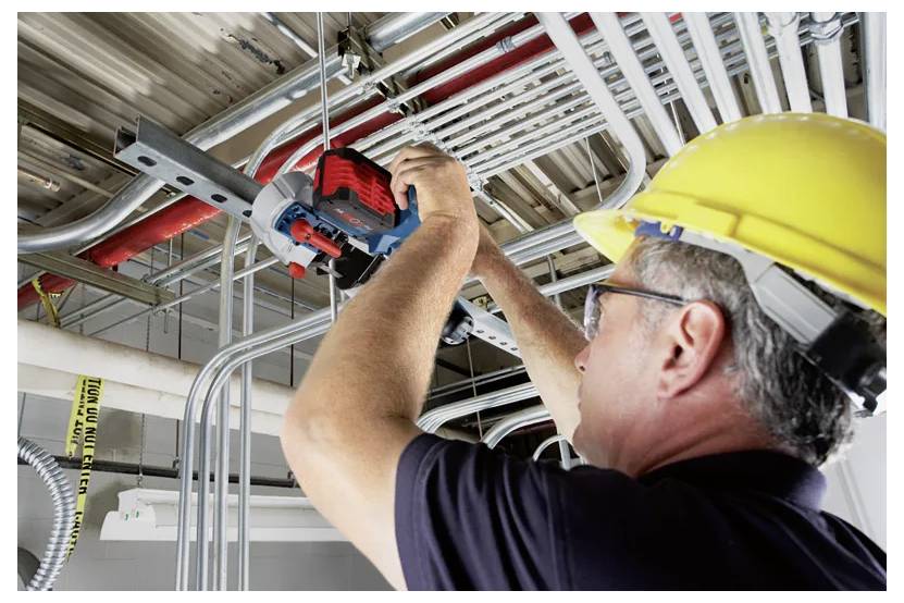 Pracownik budowlany w żółtym kasku ochronnym używa narzędzia elektrycznego do instalacji przewodu elektrycznego na suficie w ramach konstrukcji потолка.