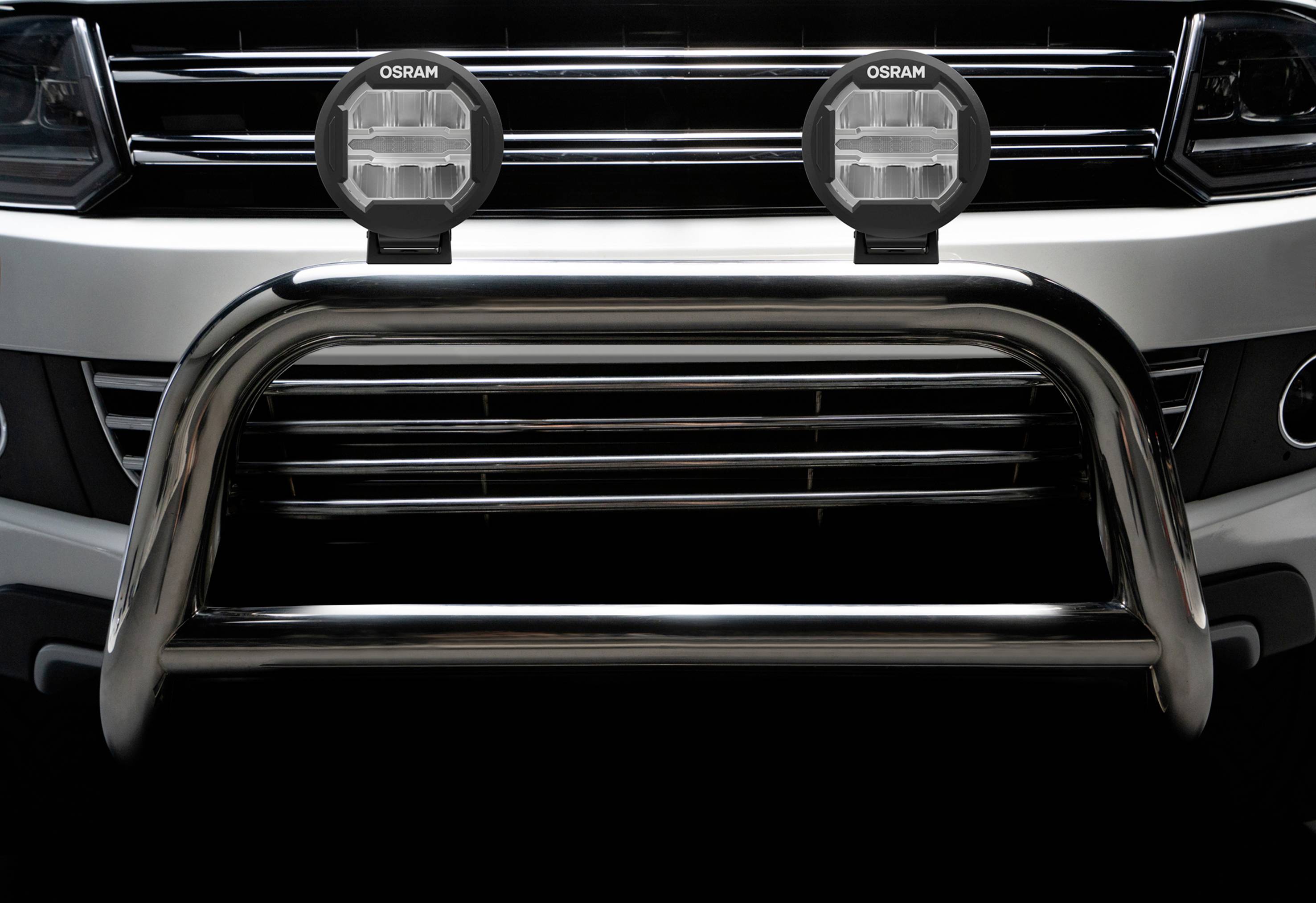 Srebrny grill zabezpieczający zamontowany na pojeździe z dwoma okrągłymi lampami dodatkowymi.