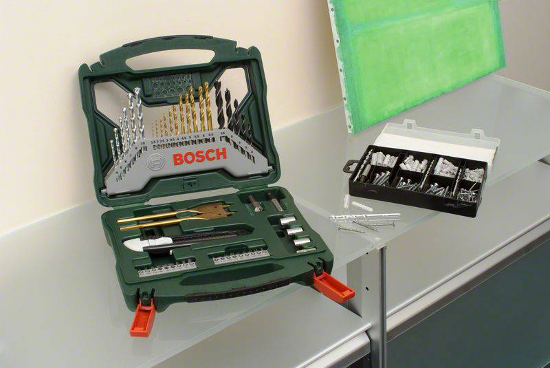 Otwarty skrzynka narzędziowa z różnymi nasadkami i wiertłami stoi na stole. Obok niej leży mniejsze pudełko ze śrubami.
