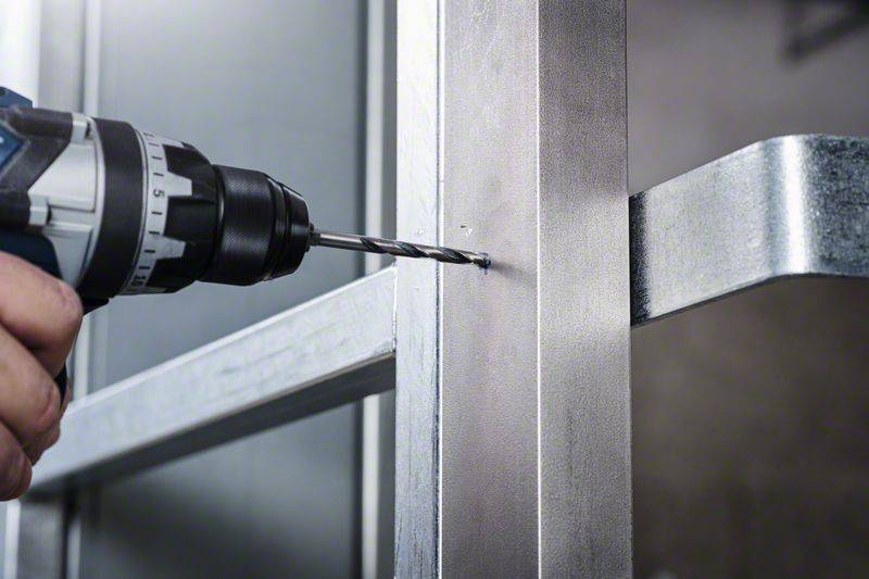 Jedna ręka trzyma elektryczną wiertarkę, która wwierca się w metalową powierzchnię. Jest to ujęcie z bliska, ukazujące samą czynność.