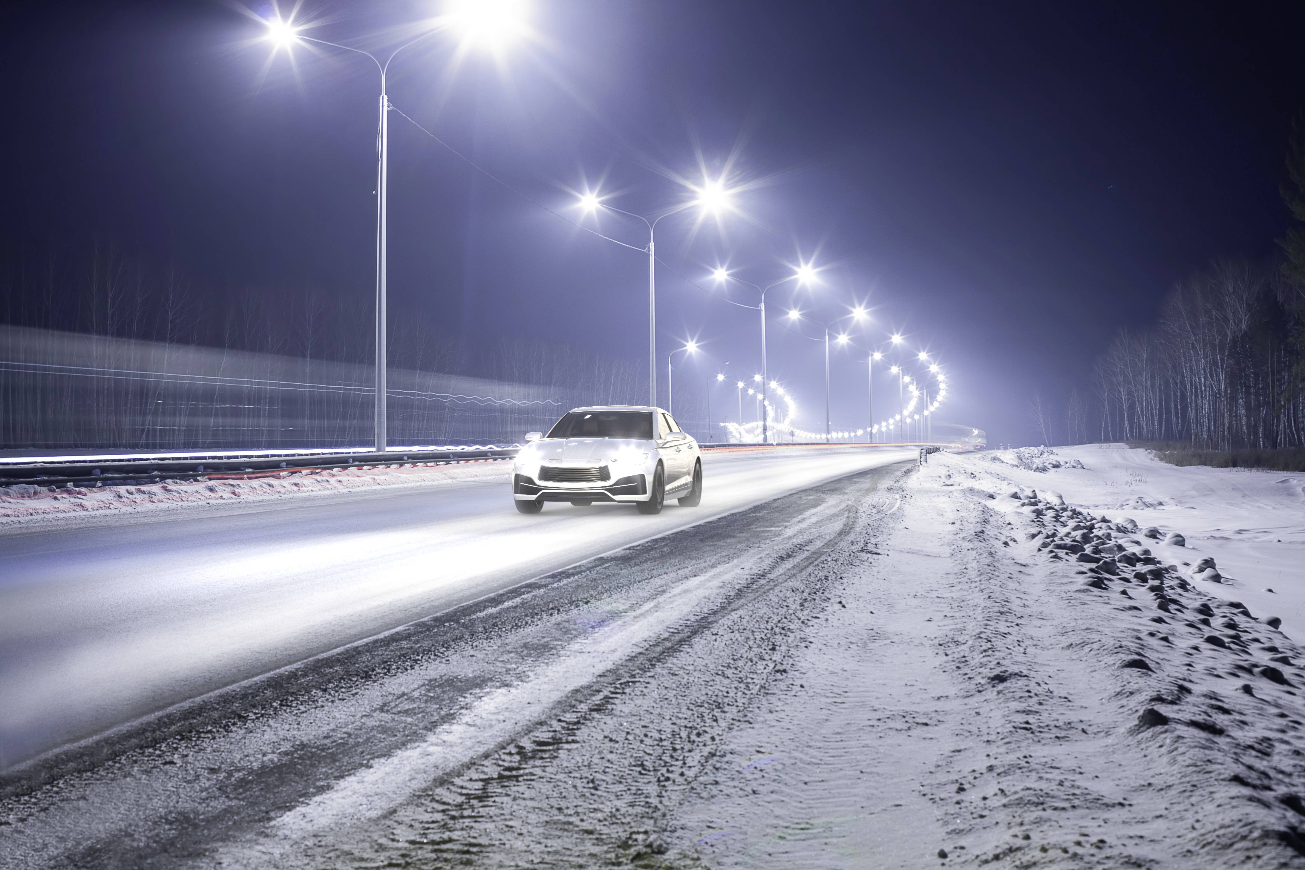 Samochód jedzie nocą po zaśnieżonej autostradzie, otoczony latarniami, które jasno oświetlają drogę.