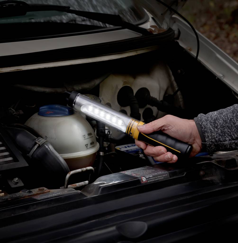 Osoba świeci przenośną lampą LED w komorę silnika samochodu, aby przeprowadzić ewentualne prace konserwacyjne.