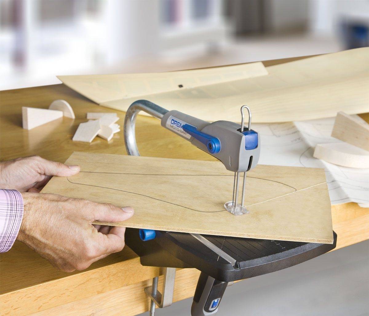 Osoba przecina płytę sklejki wyrzynarką wzdłuż narysowanego kształtu na stole.