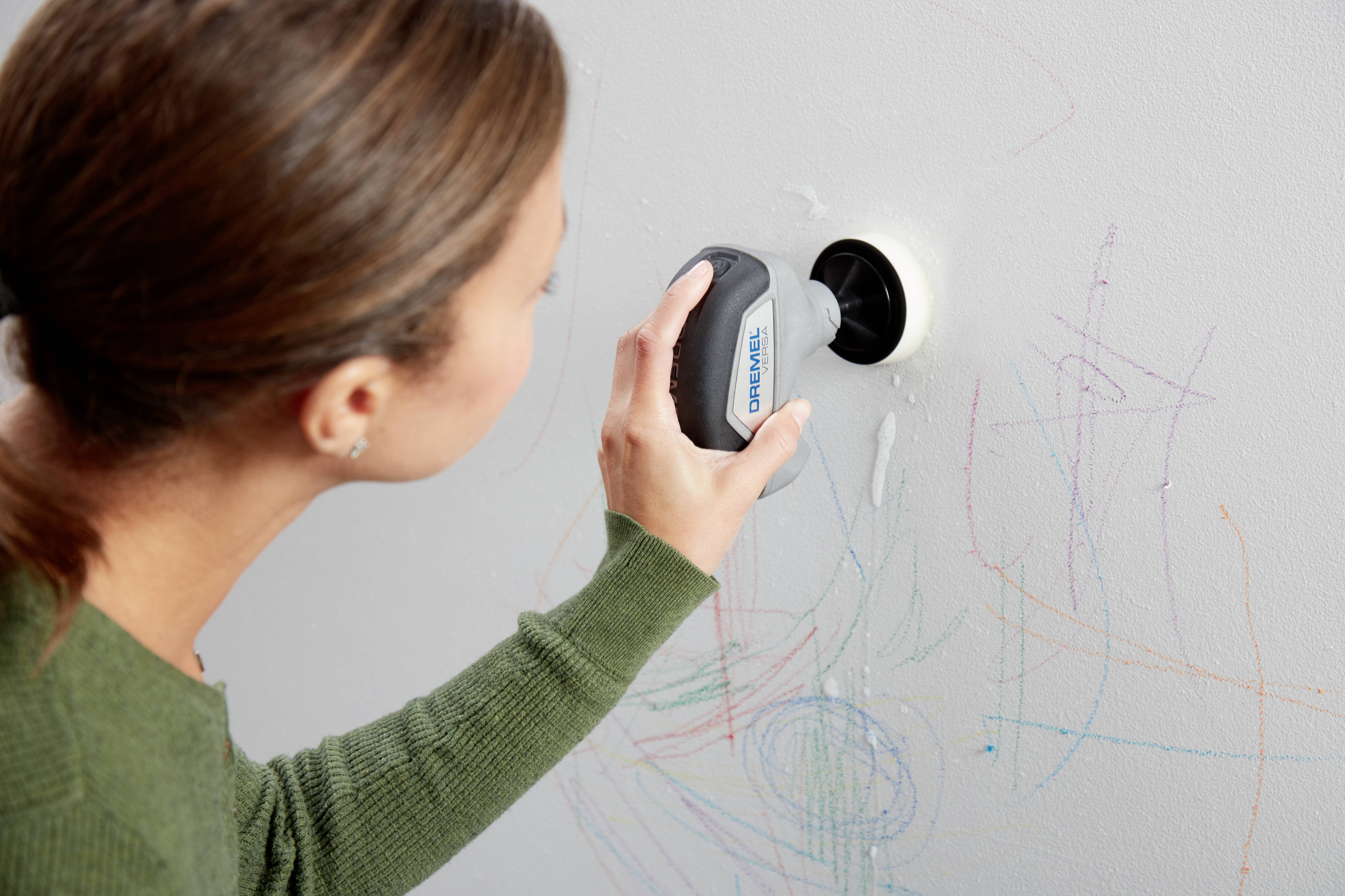 Osoba usuwa kolorowe bazgroły z ściany małym urządzeniem.