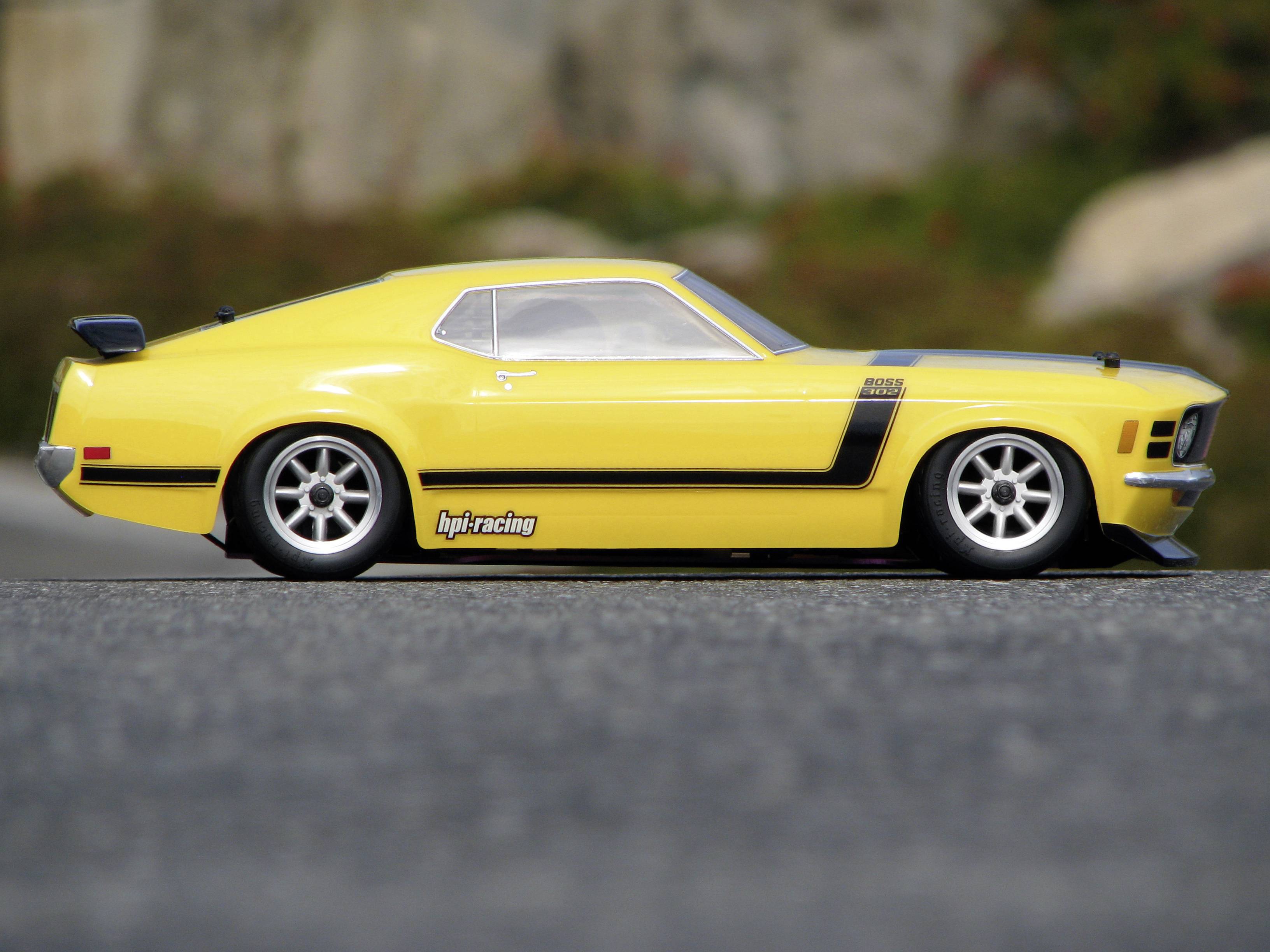 Żółty modelowy samochód sportowy na asfaltowej drodze, widok z boku. W tle rozmyty krajobraz przyrodniczy.