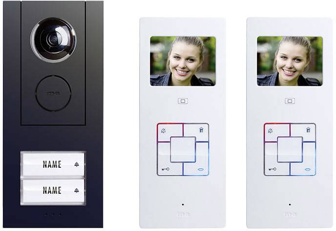 System wideodomofonowy z kamerą i dwoma białymi monitorami. Monitory wyświetlają obraz uśmiechniętej kobiety. Na dole tabliczka z nazwiskiem.