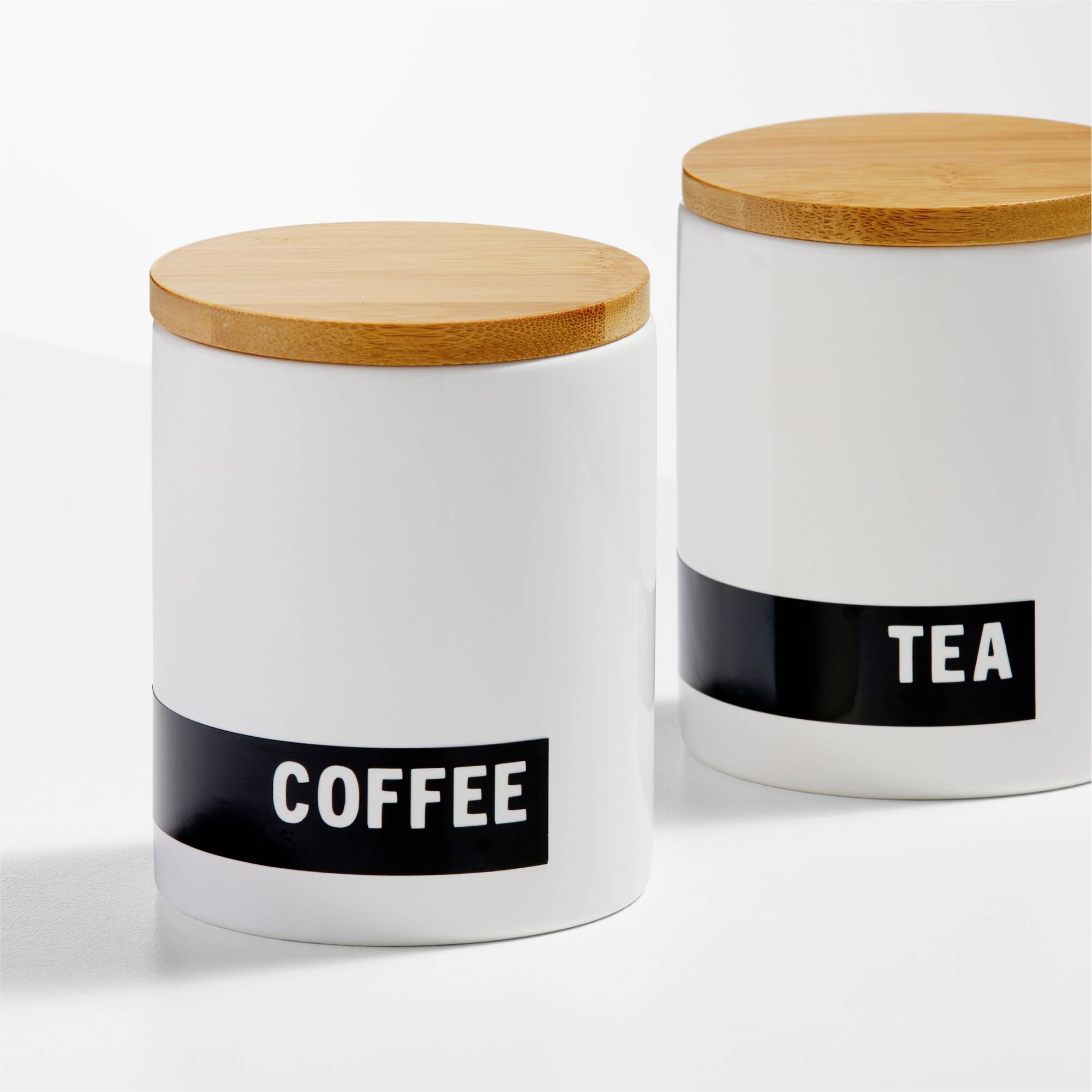 Dwie białe pojemniki do przechowywania z drewnianymi pokrywkami; lewy pojemnik jest opisany napisem 'COFFEE', prawy napisem 'TEA'.
