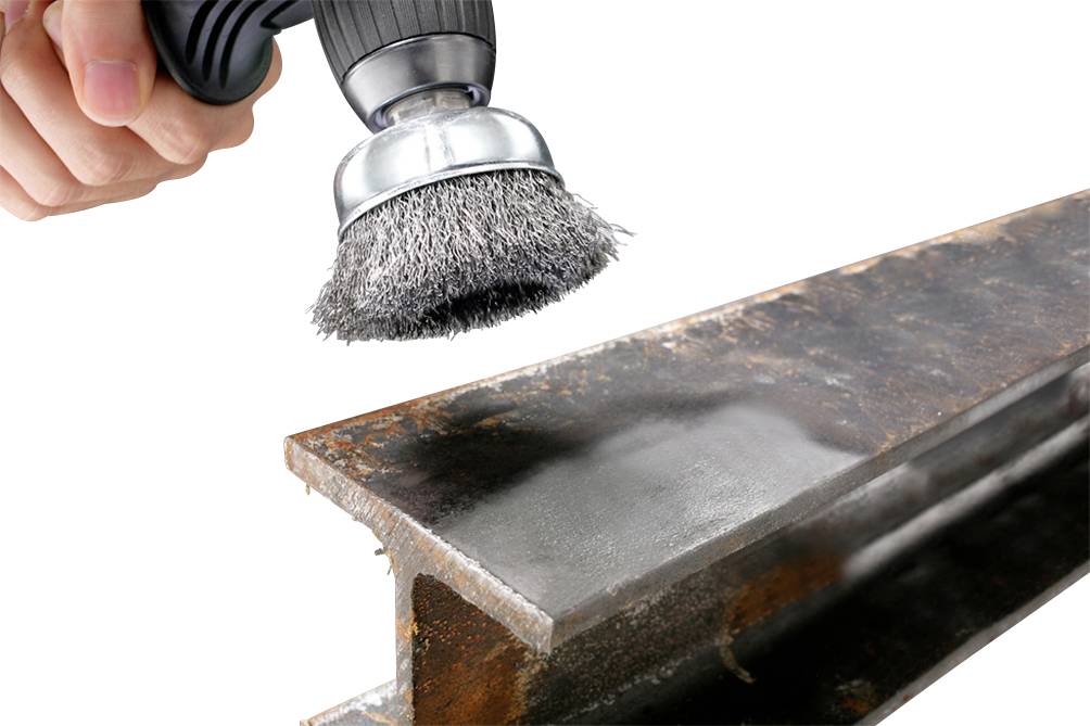 Jedna ręka trzyma szczotkę drucianą, która poleruje metal, usuwając rdzę. Zbliżenie procesu szczotkowania na górnej powierzchni metalowej belki.