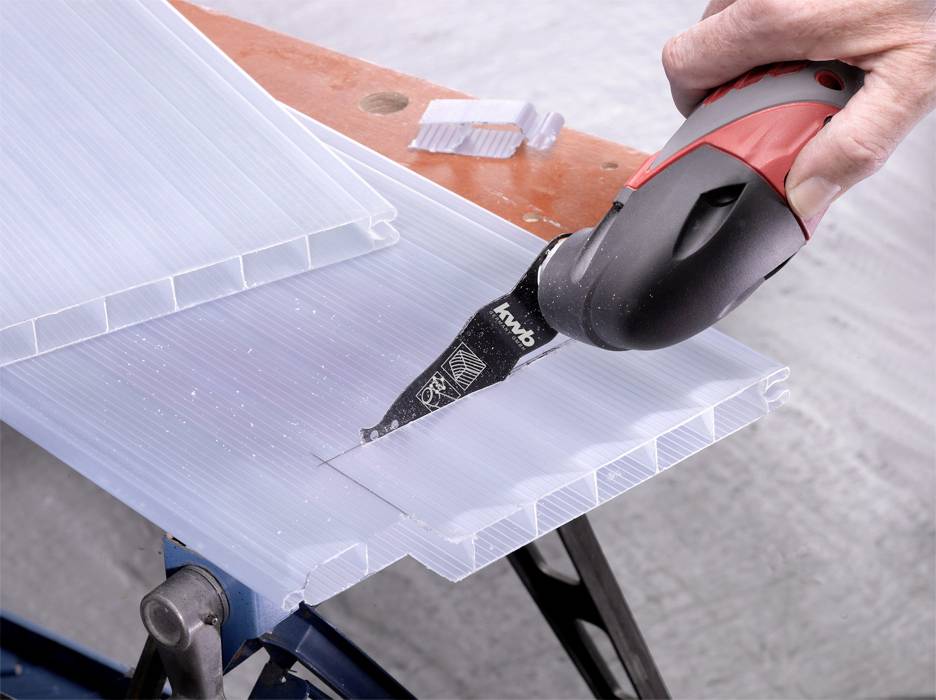 Jedna ręka trzyma elektryczną piłę, która przecina kawałek przezroczystego materiału z tworzywa sztucznego.
