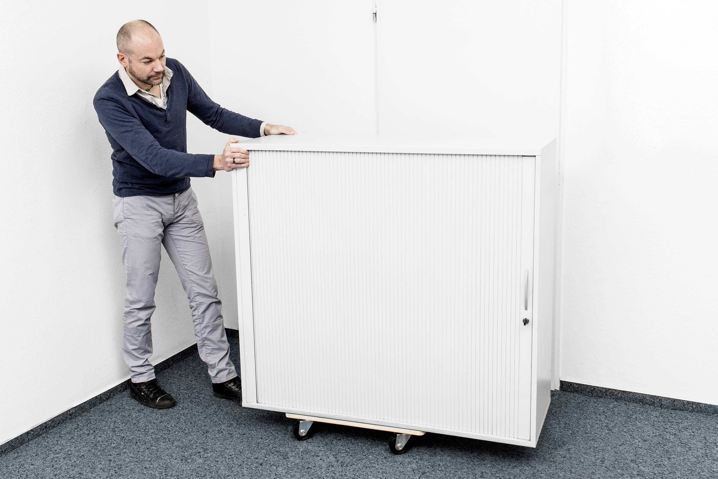 Osoba w biurze przesuwa biały kontener na kółkach.