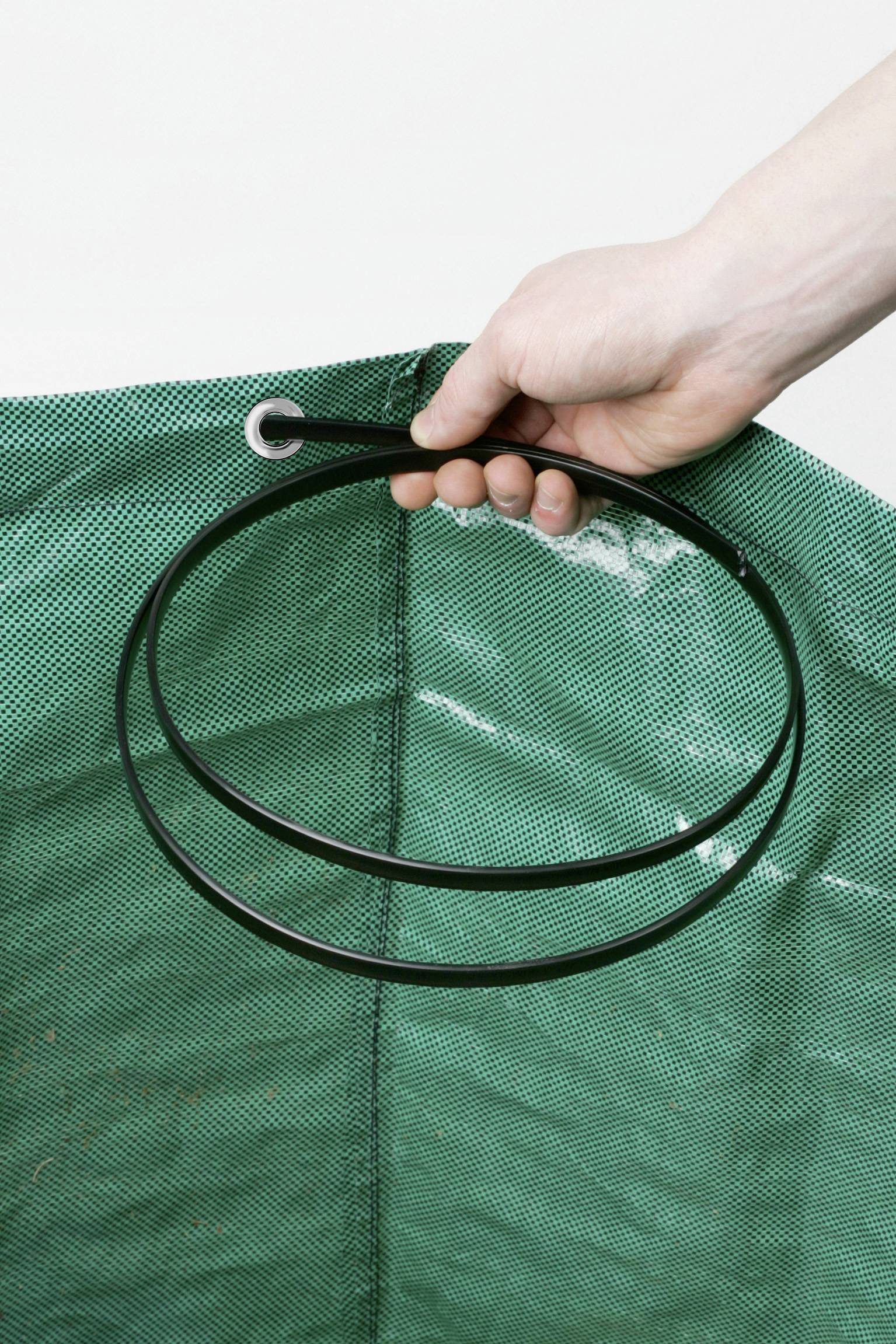 Ręka trzyma czarny metalowy pierścień nad zieloną siatką.