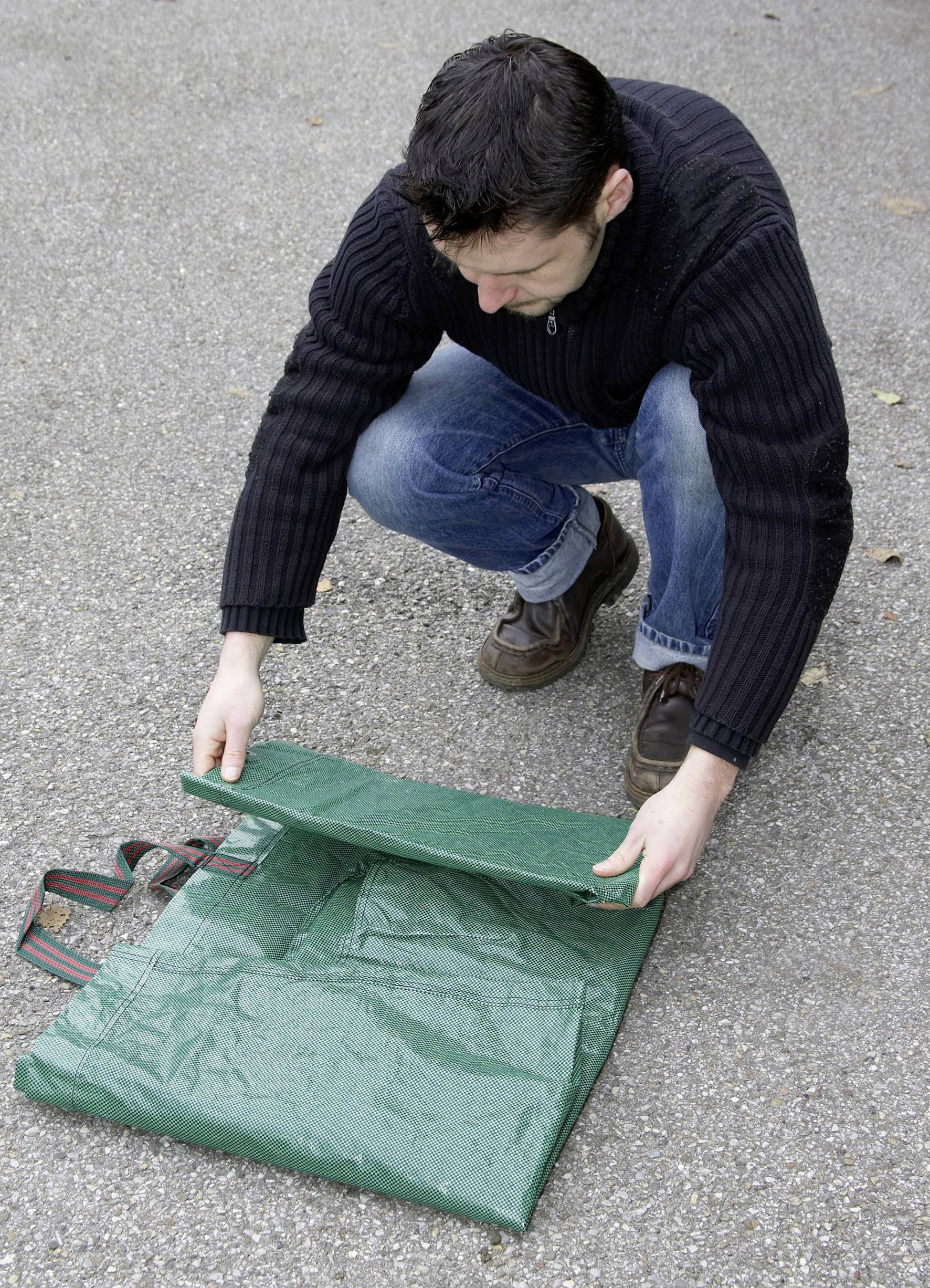 Mężczyzna klęczy na dworze i składa zieloną plandekę na asfaltowej nawierzchni.