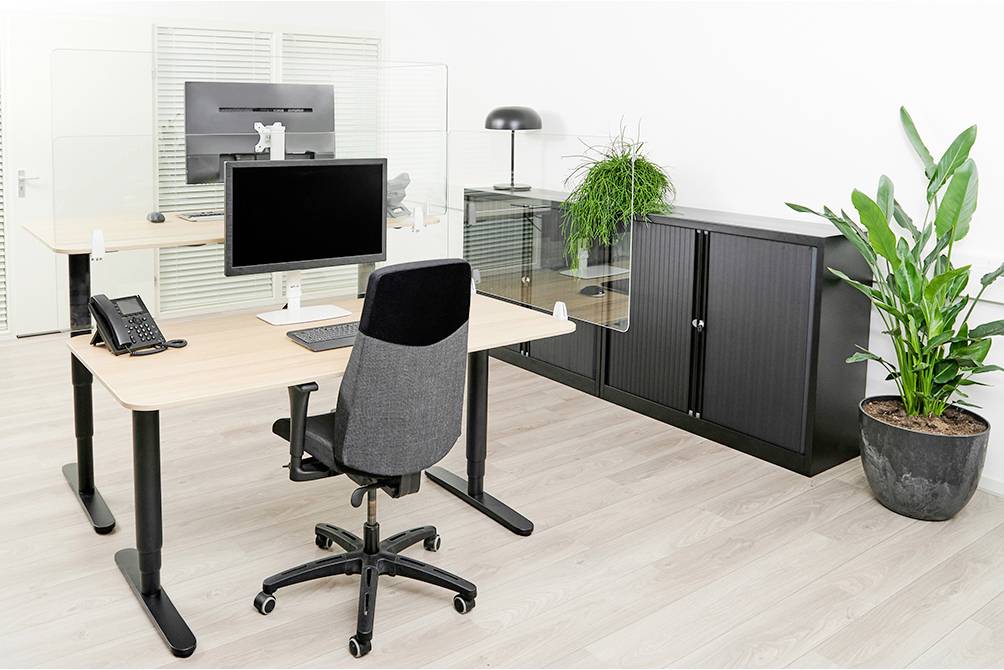 Nowoczesne biuro z dwoma biurkami, krzesłem, monitorem, roślinami i czarną szafką na dokumenty przed białą ścianą.