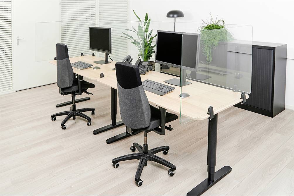 Nowoczesna przestrzeń biurowa z dwoma biurkami, po dwa krzesła przy każdym, komputerami i zielonymi roślinami. Szklane przegrody oddzielają stanowiska pracy.