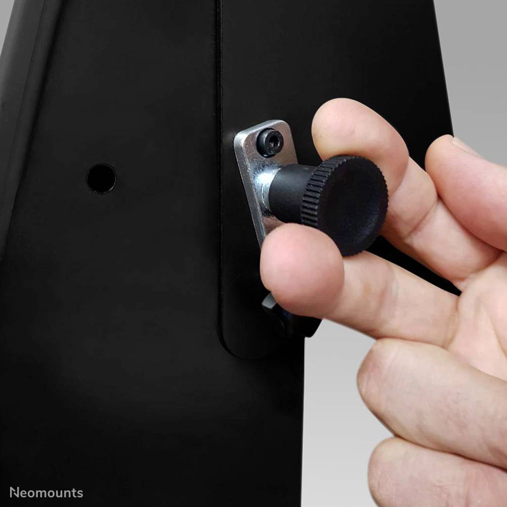 Ręka obraca śrubę regulacyjną na czarnym urządzeniu, zmieniając jego pozycję lub napięcie.