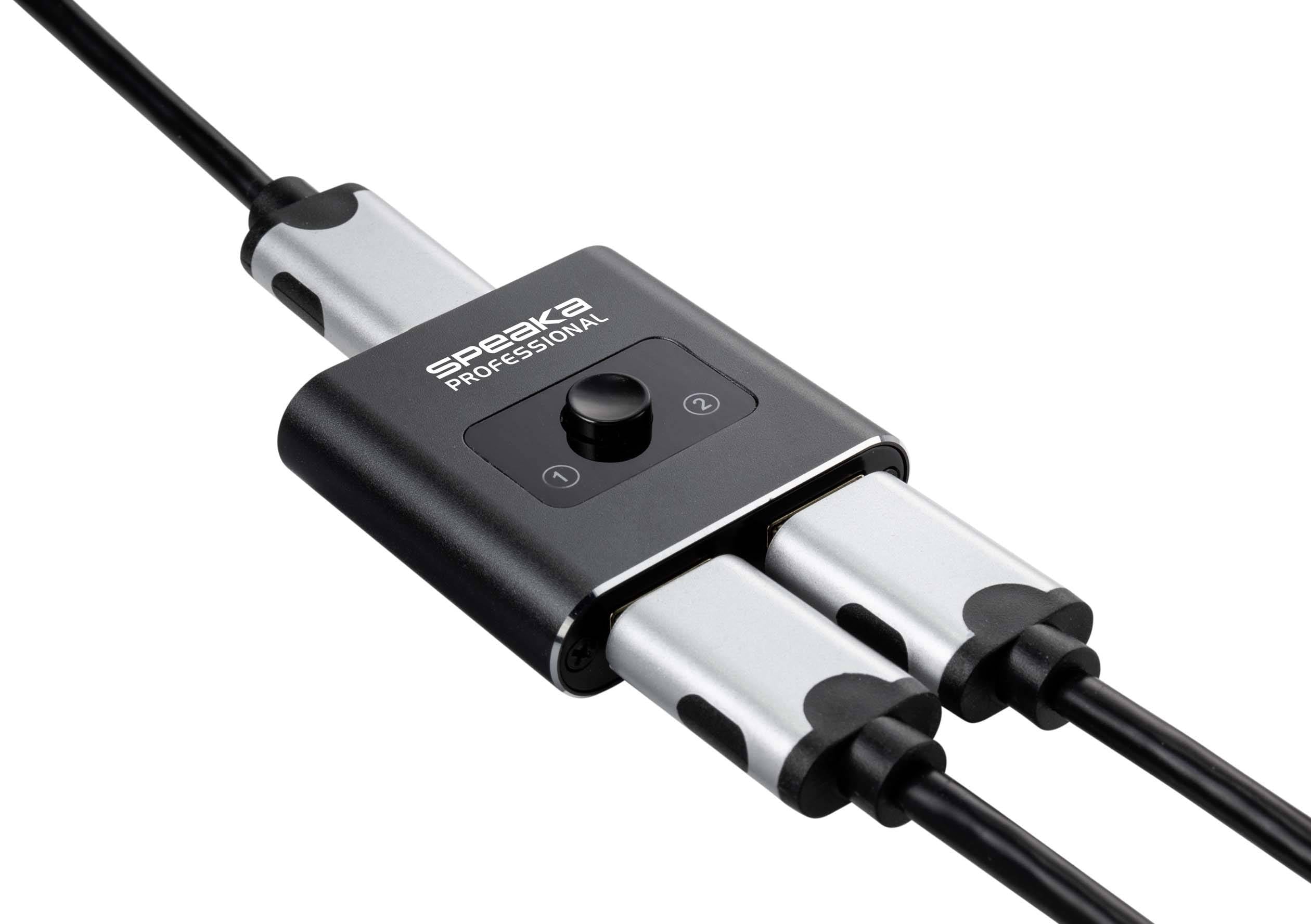 Czarny, prostokątny elektroniczny przełącznik z napisem 'SPEAKA PROFESSIONAL' pośrodku, podłączony do kilku kabli.
