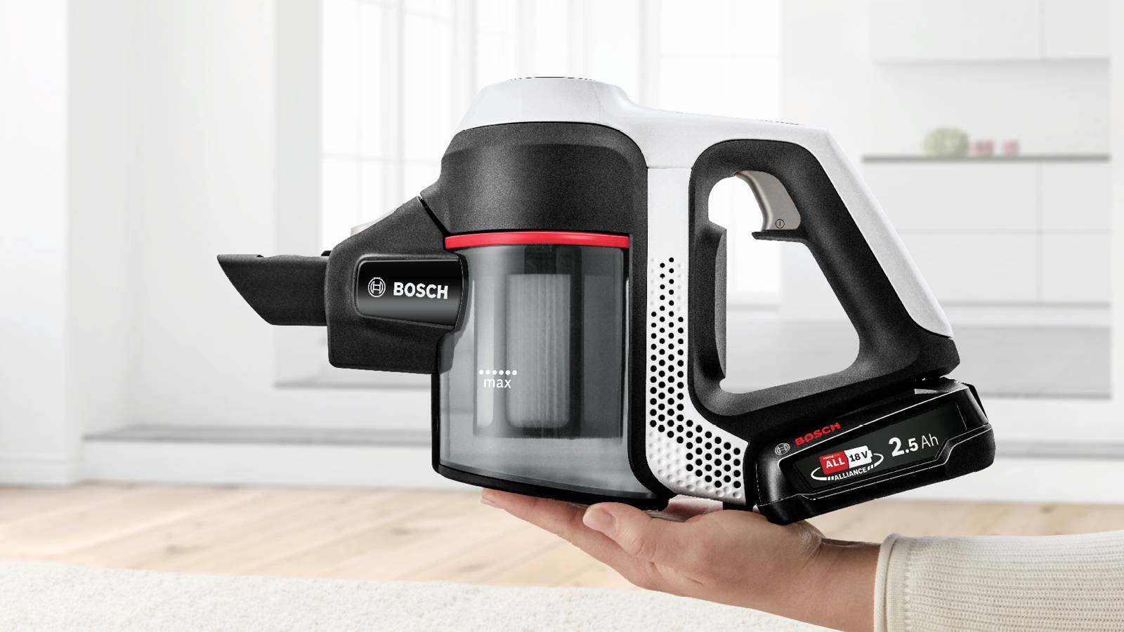 Trzymając w ręku kompaktowy odkurzacz akumulatorowy, prezentuje on designerskie szczegóły marki Bosch na tle nowocześnie urządzonego pomieszczenia.