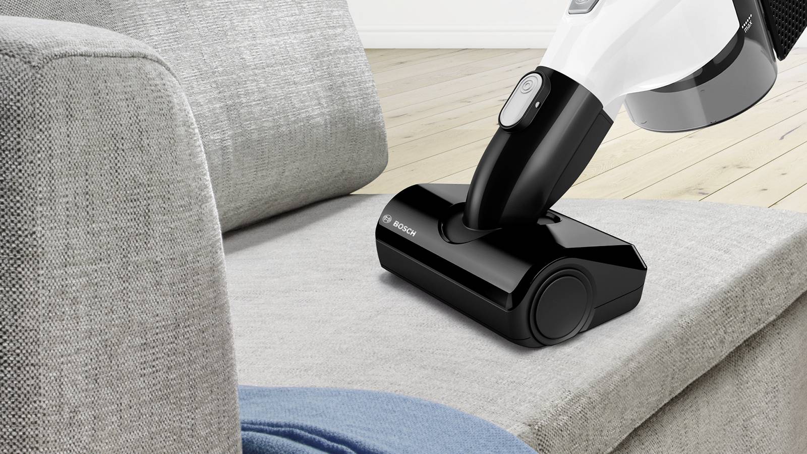 Bezprzewodowy odkurzacz czyści szarą powierzchnię kanapy w salonie. Drewniana podłoga w tle.