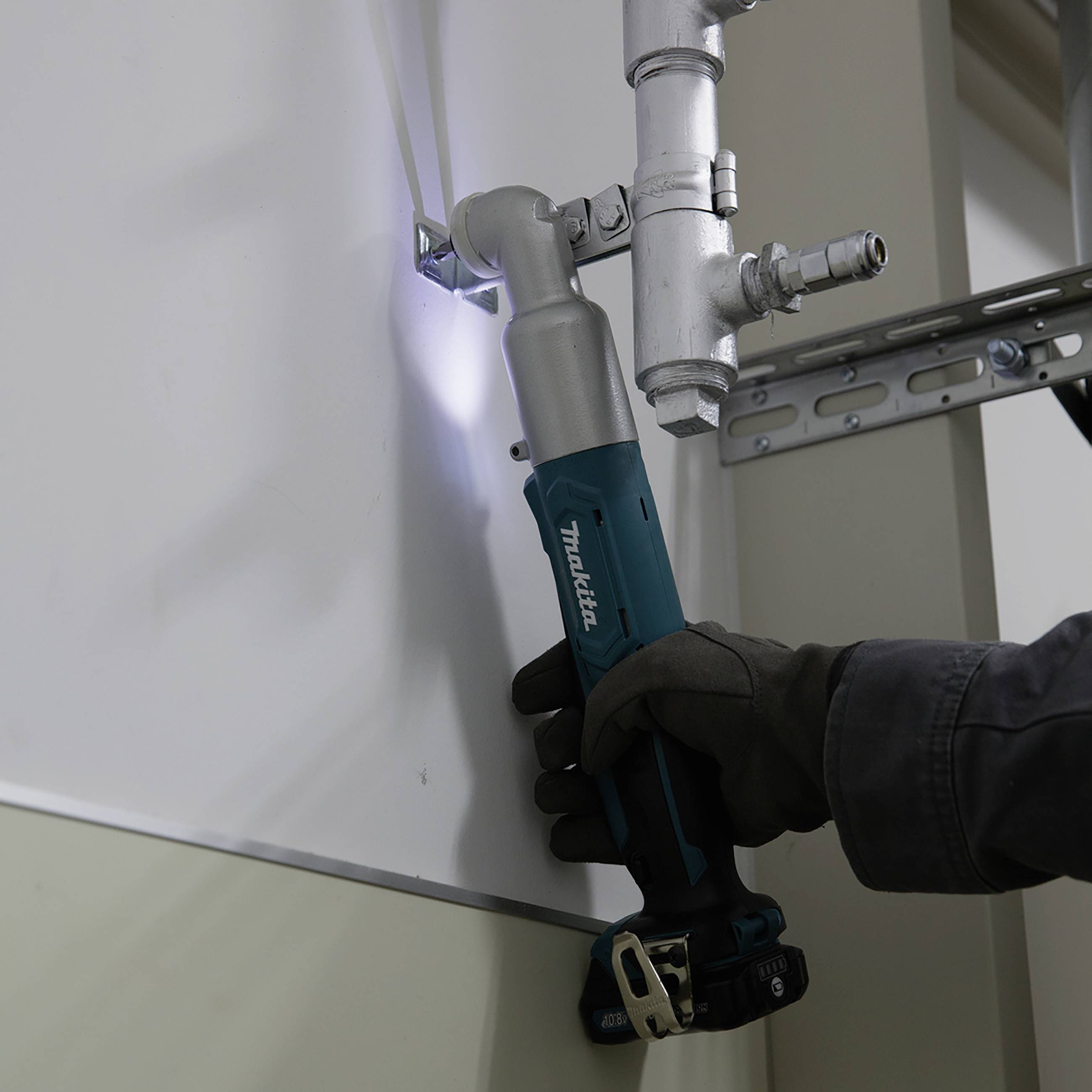 Osoba montuje metalową rurę na ścianie za pomocą wiertarki. Osoba nosi rękawice ochronne.