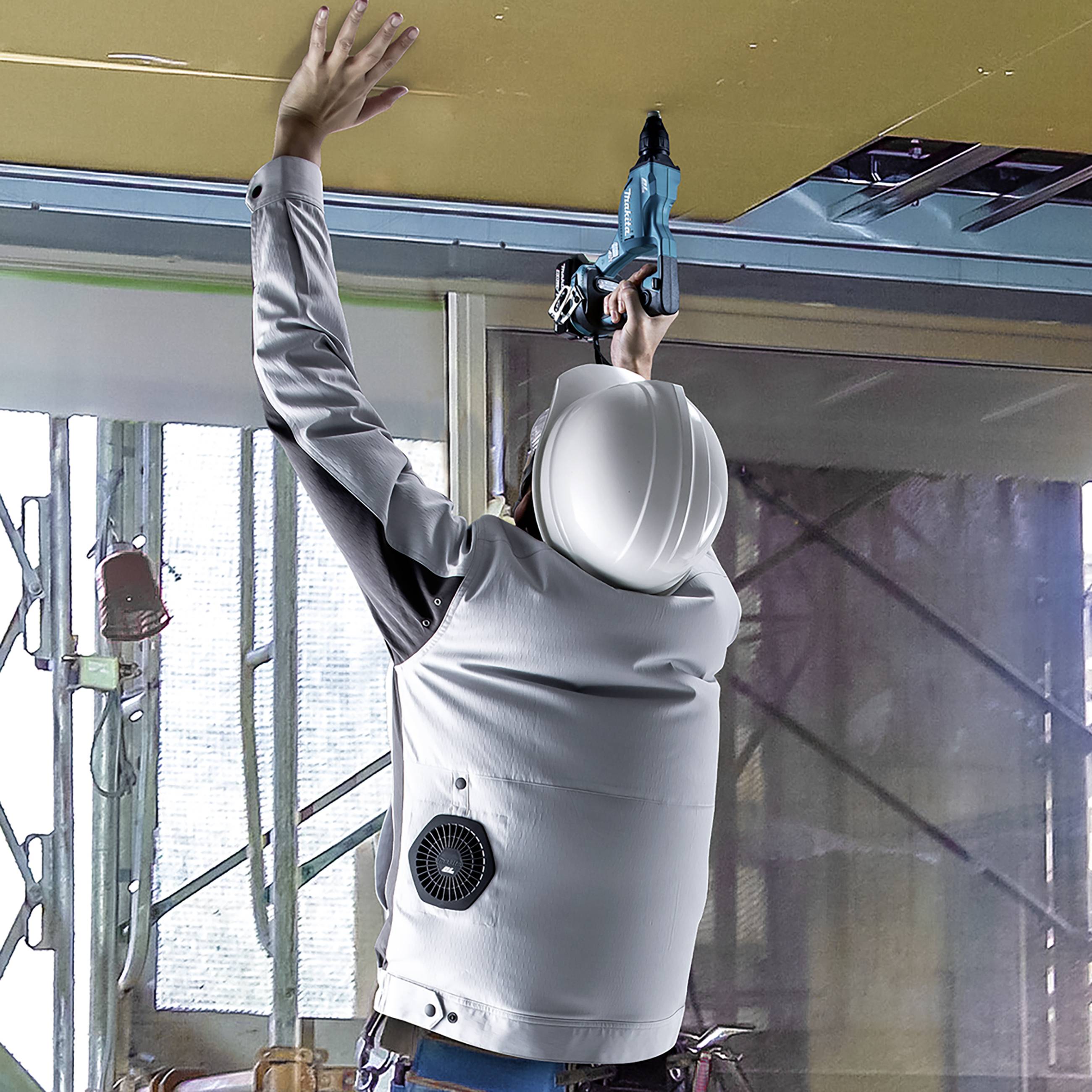 Osoba w ubraniu roboczym i kasku montuje sufit za pomocą elektronarzędzia na placu budowy.