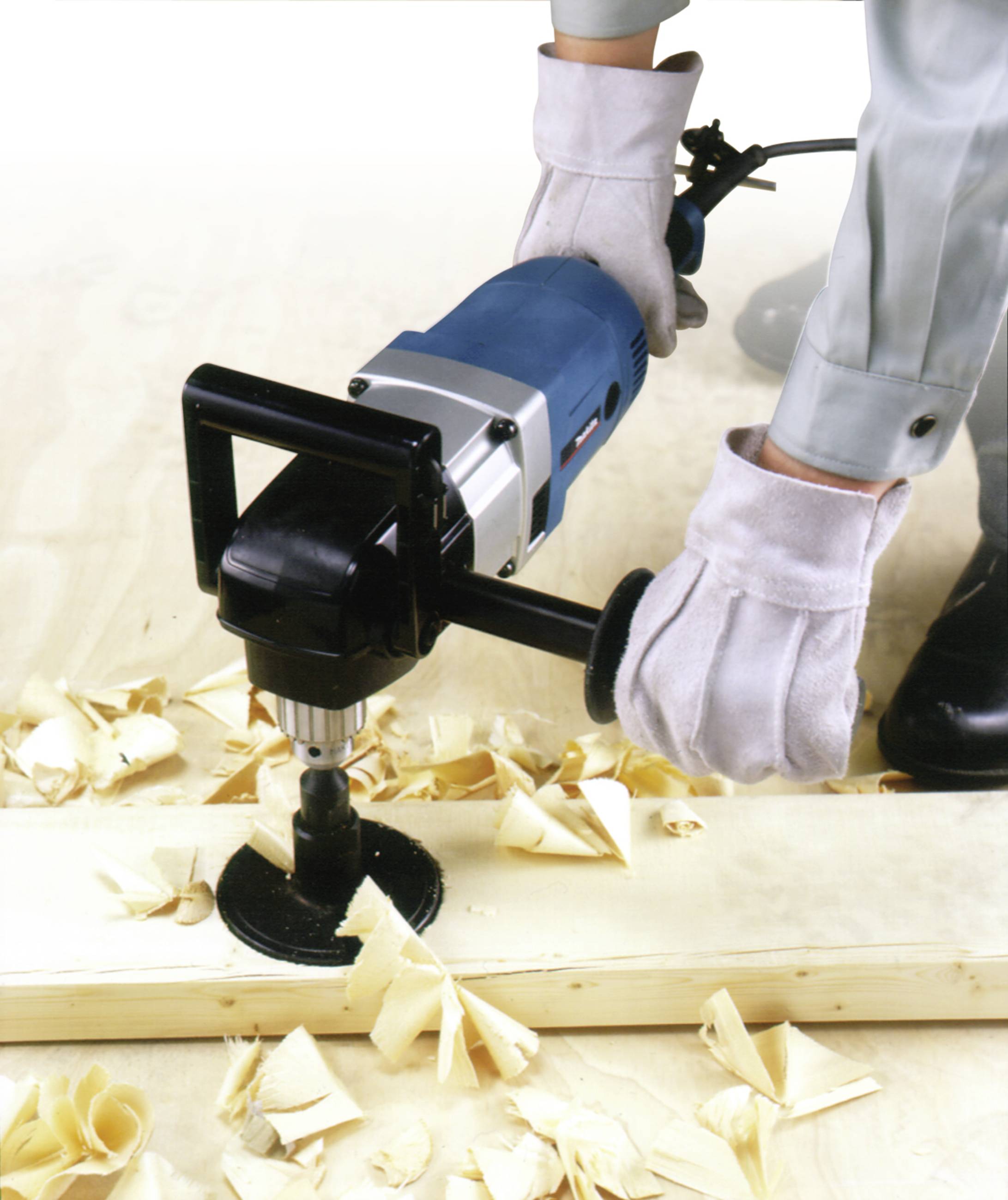 Osoba obsługuje elektryczne narzędzie wiertnicze na desce drewnianej, a wokół elementu roboczego są rozrzucone wióry.