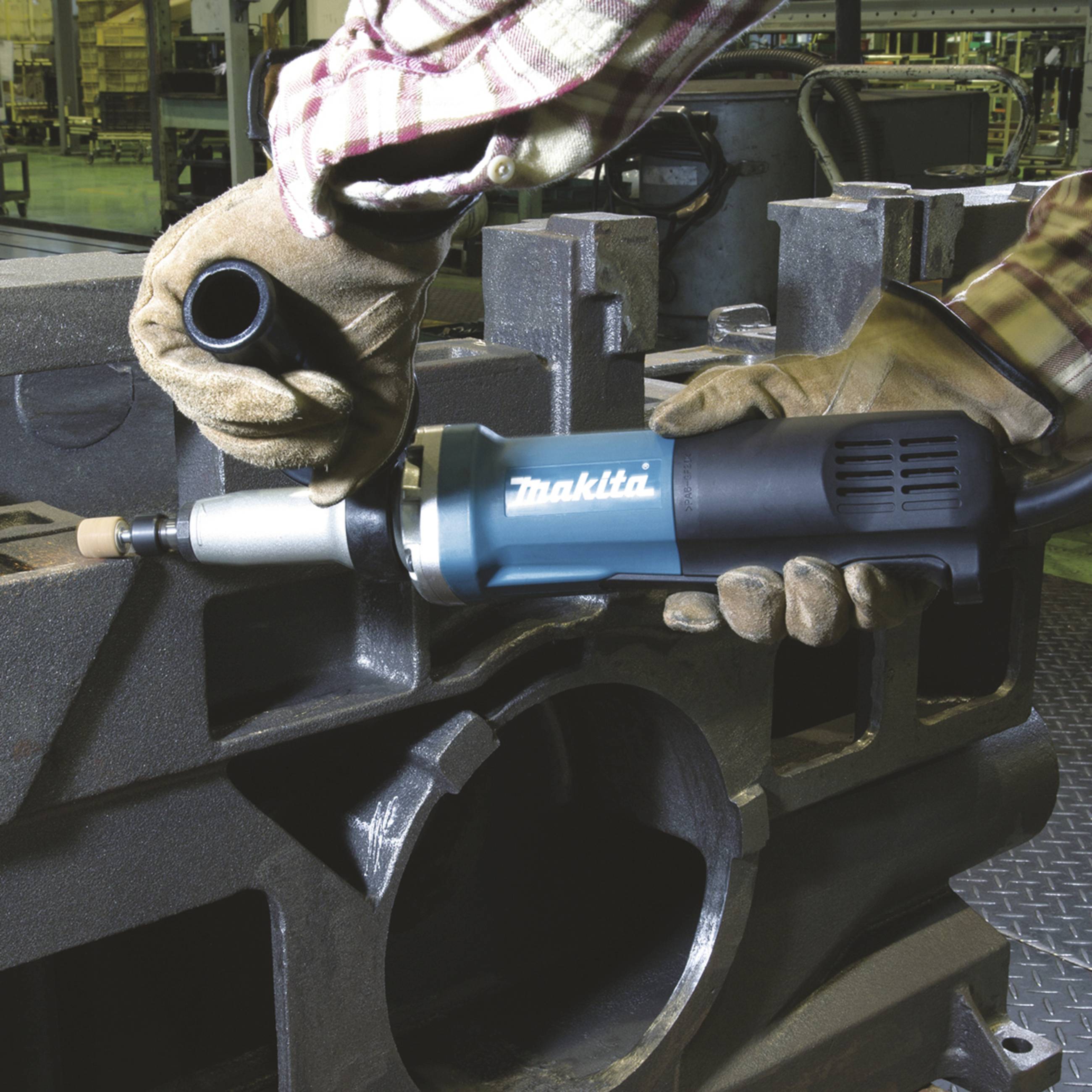 Osoba ubrana w strój roboczy używa elektrycznego narzędzia szlifierskiego do obróbki metalu w środowisku warsztatu.