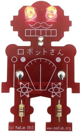 Czerwona płytka drukowana w kształcie robota z świecącymi oczami LED i japańskim napisem. Widoczne są elektroniczne komponenty.