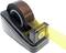 Czarna podajnik do taśmy klejącej trzymający żółtą taśmę. Podajnik wykonany jest z tworzywa sztucznego z antypoślizgowym spodem.