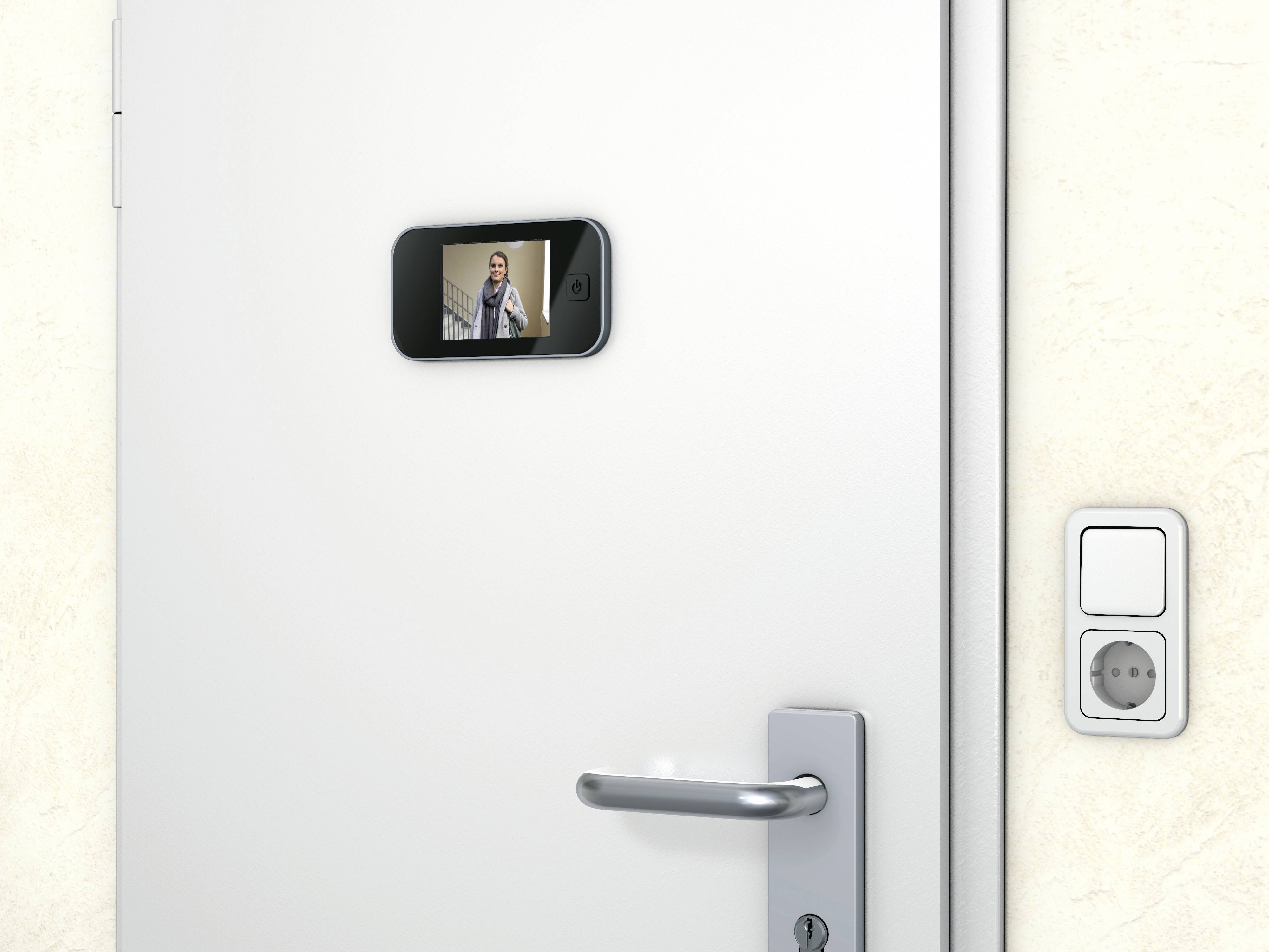 Smartfon wisi u drzwi jak cyfrowy wizjer. Na ekranie widać osobę. Obok klamki drzwiowej znajduje się włącznik światła.