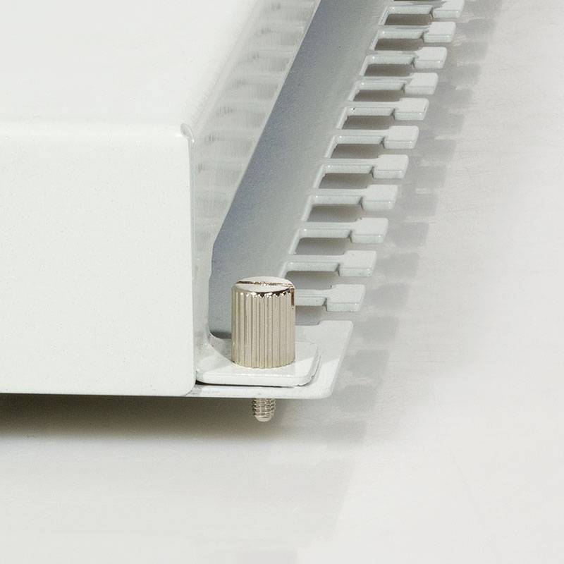 Biały grzejnik zamontowany w pomieszczeniu, z regulatorem temperatury umieszczonym z boku. Regulator pozwala na dostosowanie poziomu ciepła.