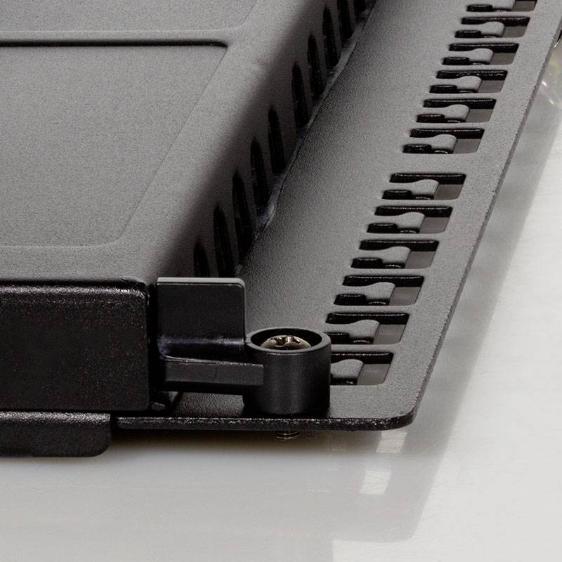 Zbliżenie czarno-srebrnego elementu komputerowego z otworami wentylacyjnymi i śrubą mocującą, leżącego na powierzchni odbijającej światło.