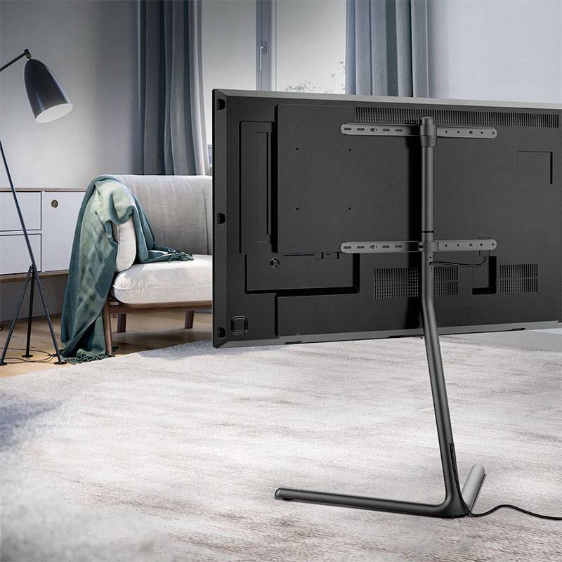 Telewizor stoi gustownie na wąskiej podstawce w nowocześnie urządzonym salonie, w tle widać sofę i lampę stojącą.