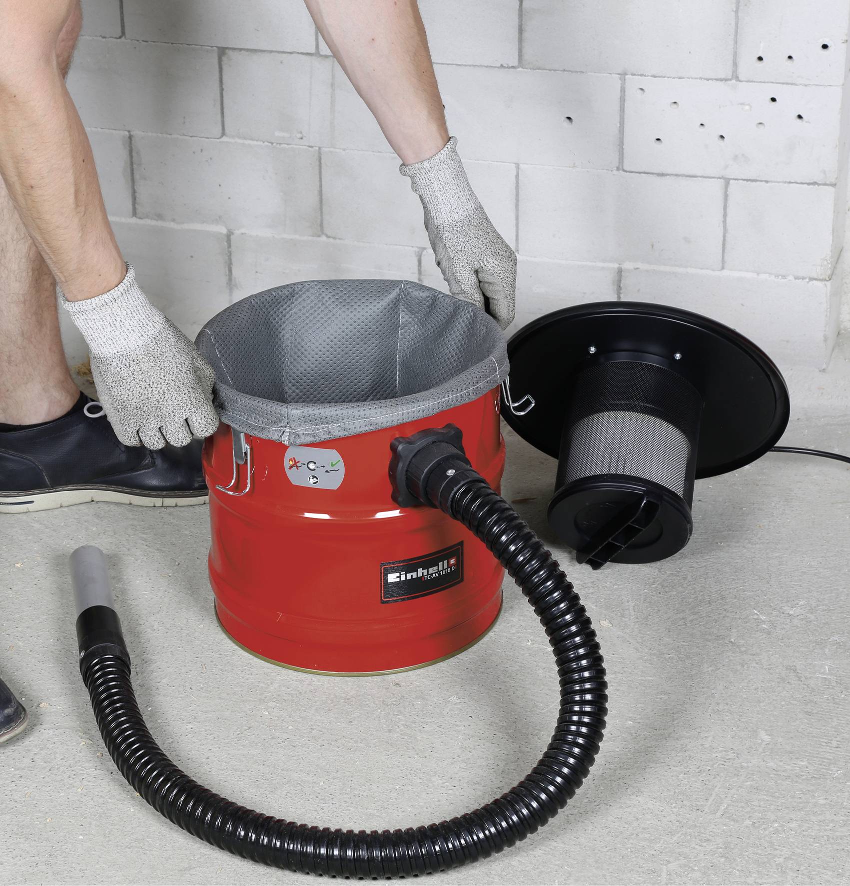 Osoba montuje odkurzacz do popiołu. Czerwony pojemnik stoi otwarty obok czarnego węża i pokrywy filtra.