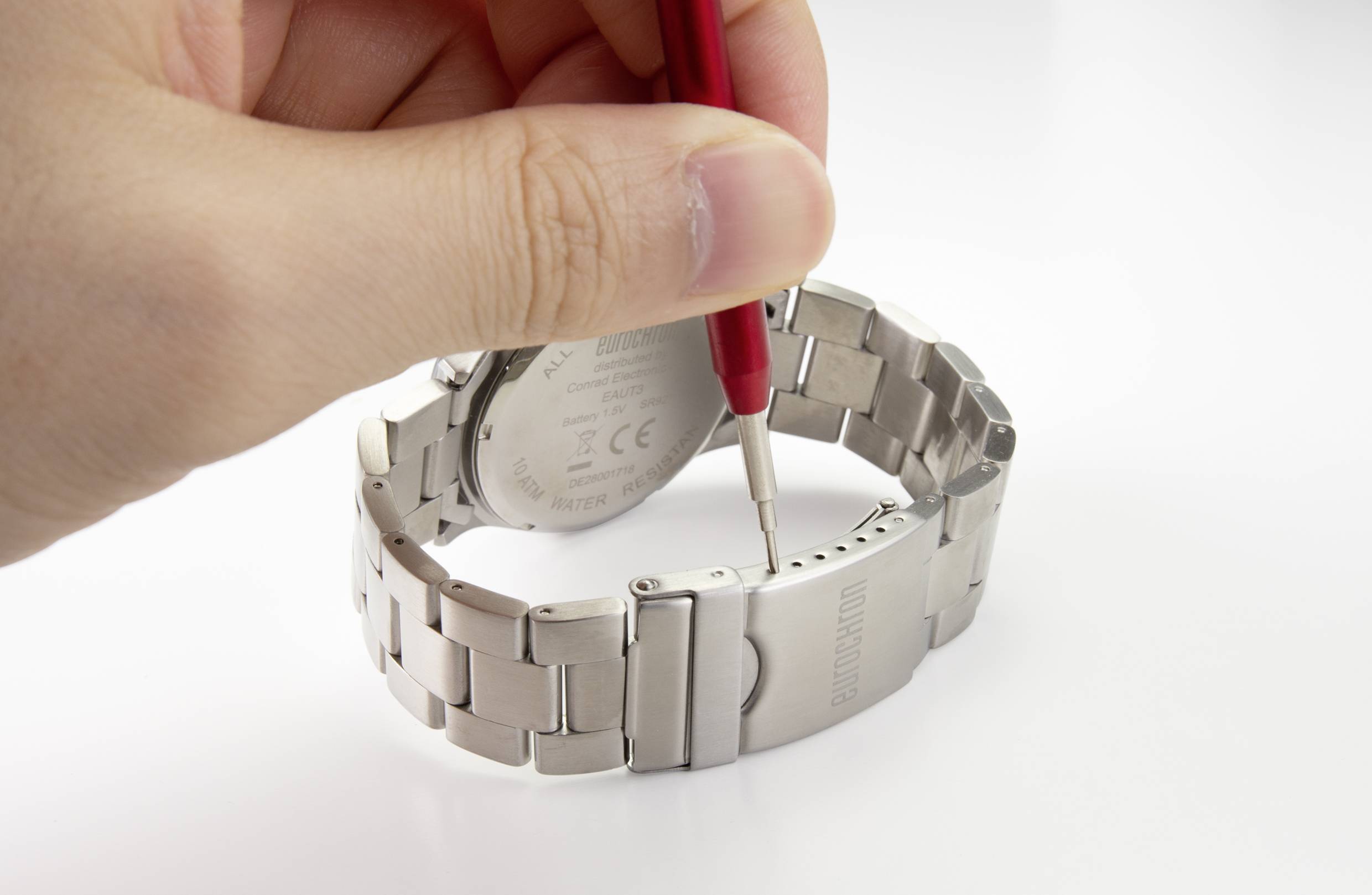 Ręka używa narzędzia do regulacji metalowej bransolety zegarka.