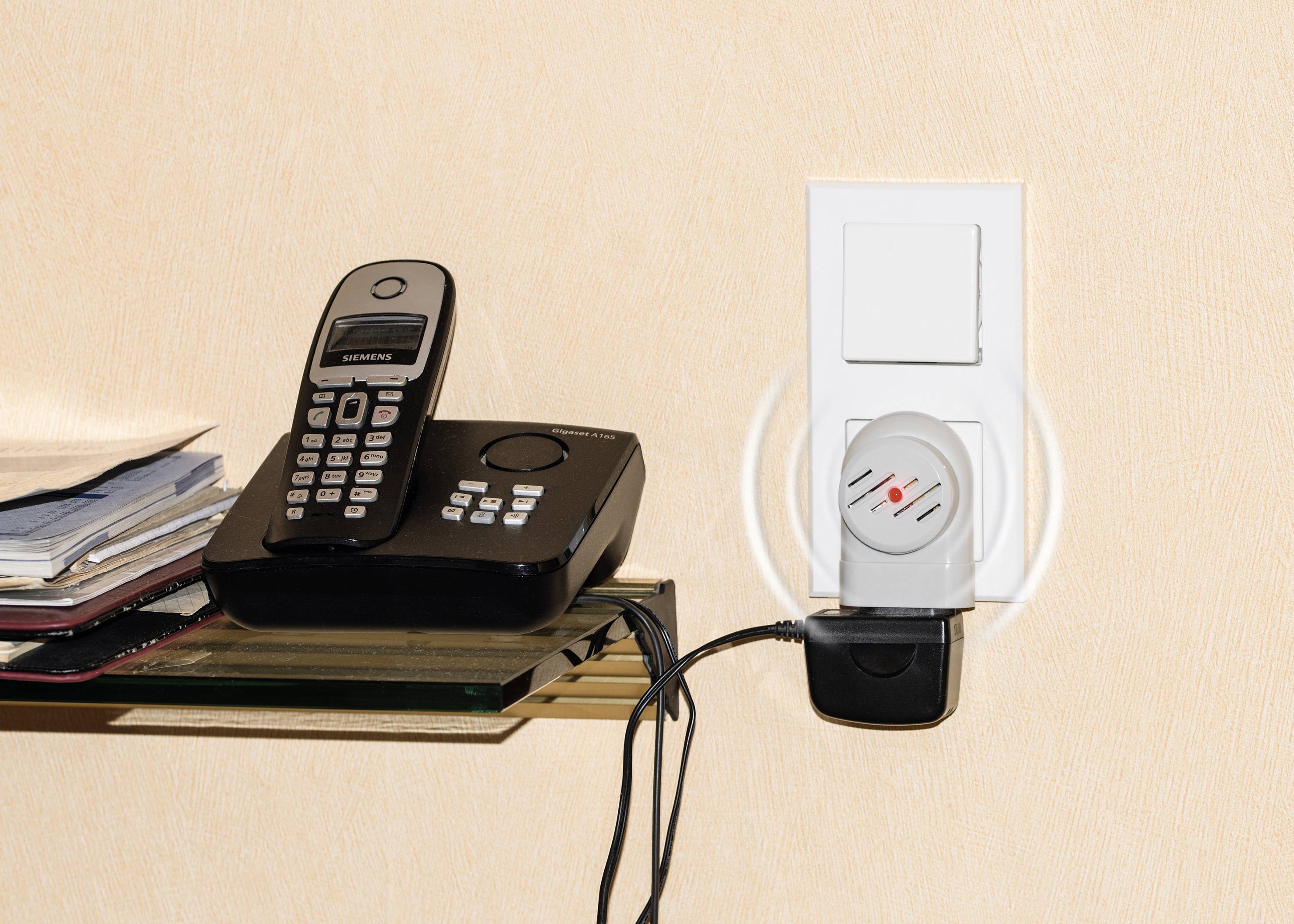 System europejskiego nadzoru czujek iskrowych' przedstawia telefon z bazą stacji obok gniazda elektrycznego z podłączonymi urządzeniami.