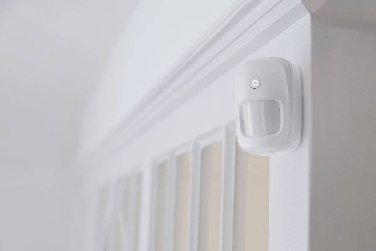Biały czujnik ruchu jest zamontowany na ścianie obok drzwi, aby wykrywać ruch w pomieszczeniu.