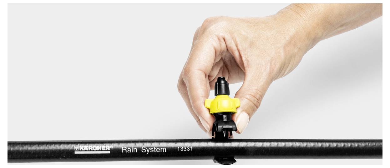 Dłoń osoby reguluje dyszę na czarnym wężu oznaczonym etykietą "Karcher Rain System 13333".