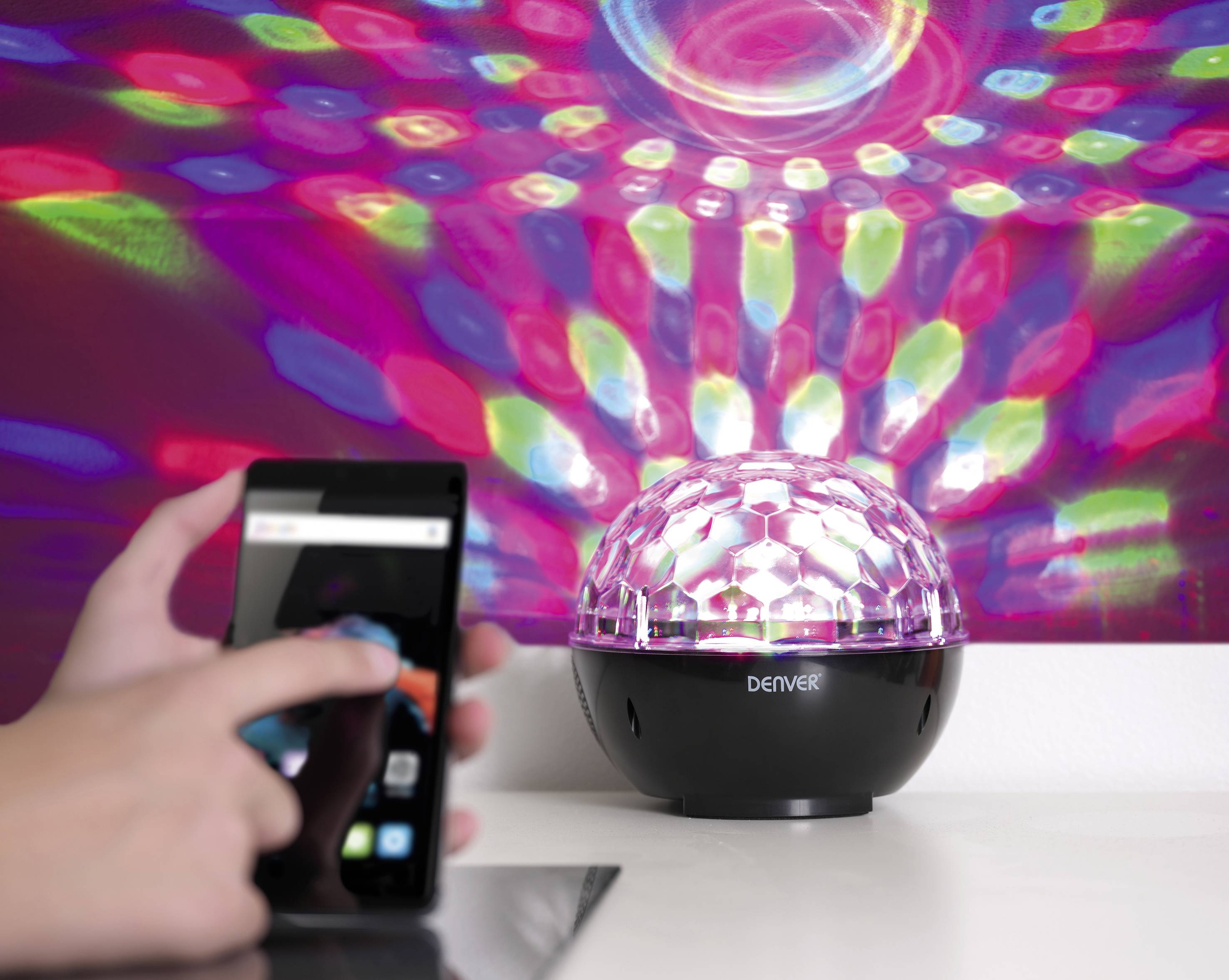 Kolorowa lampa rzuca wzory na ścianę. Jedna osoba obsługuje smartfona.